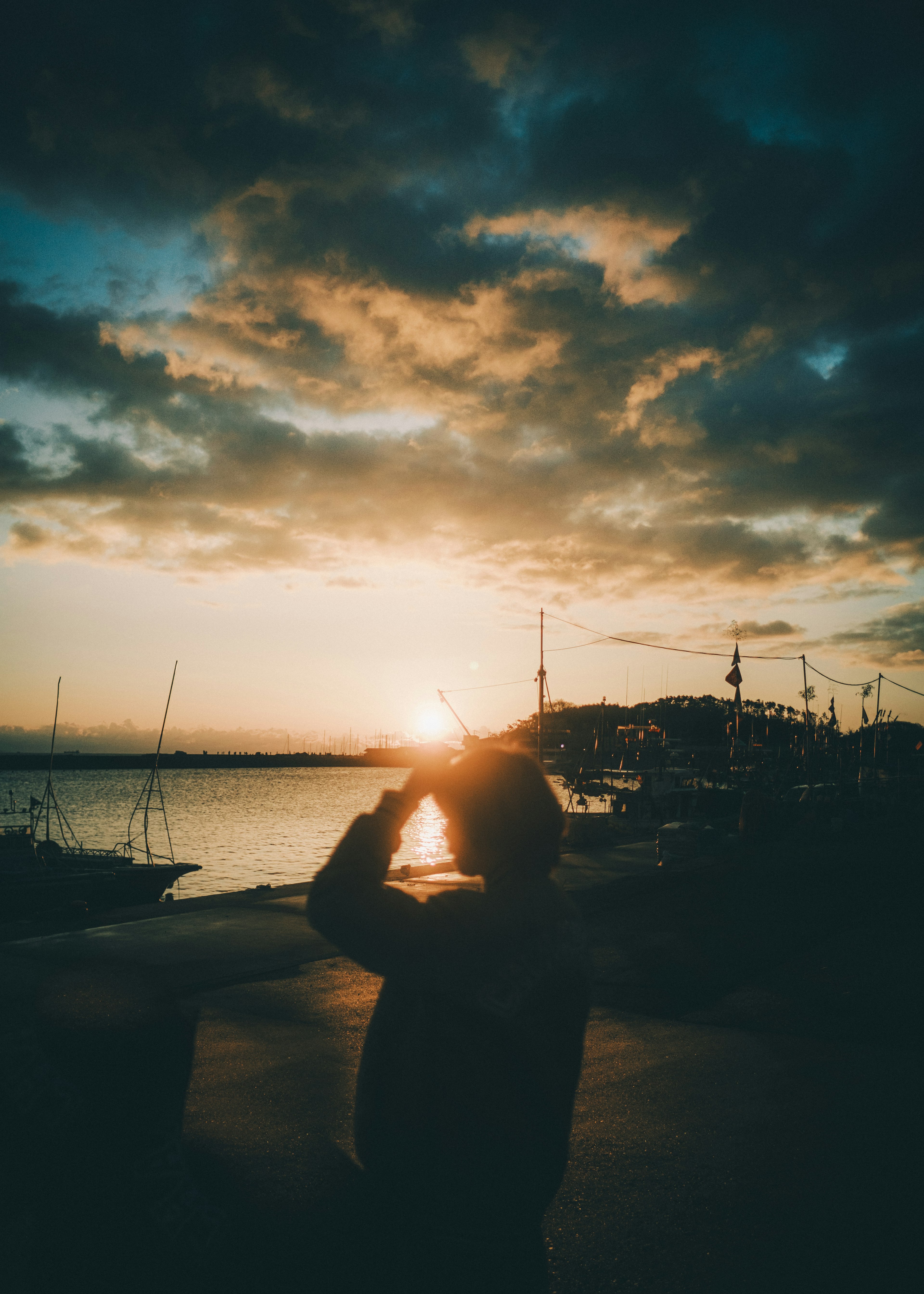 Silhouette di una persona che alza le mani contro un tramonto sull'acqua