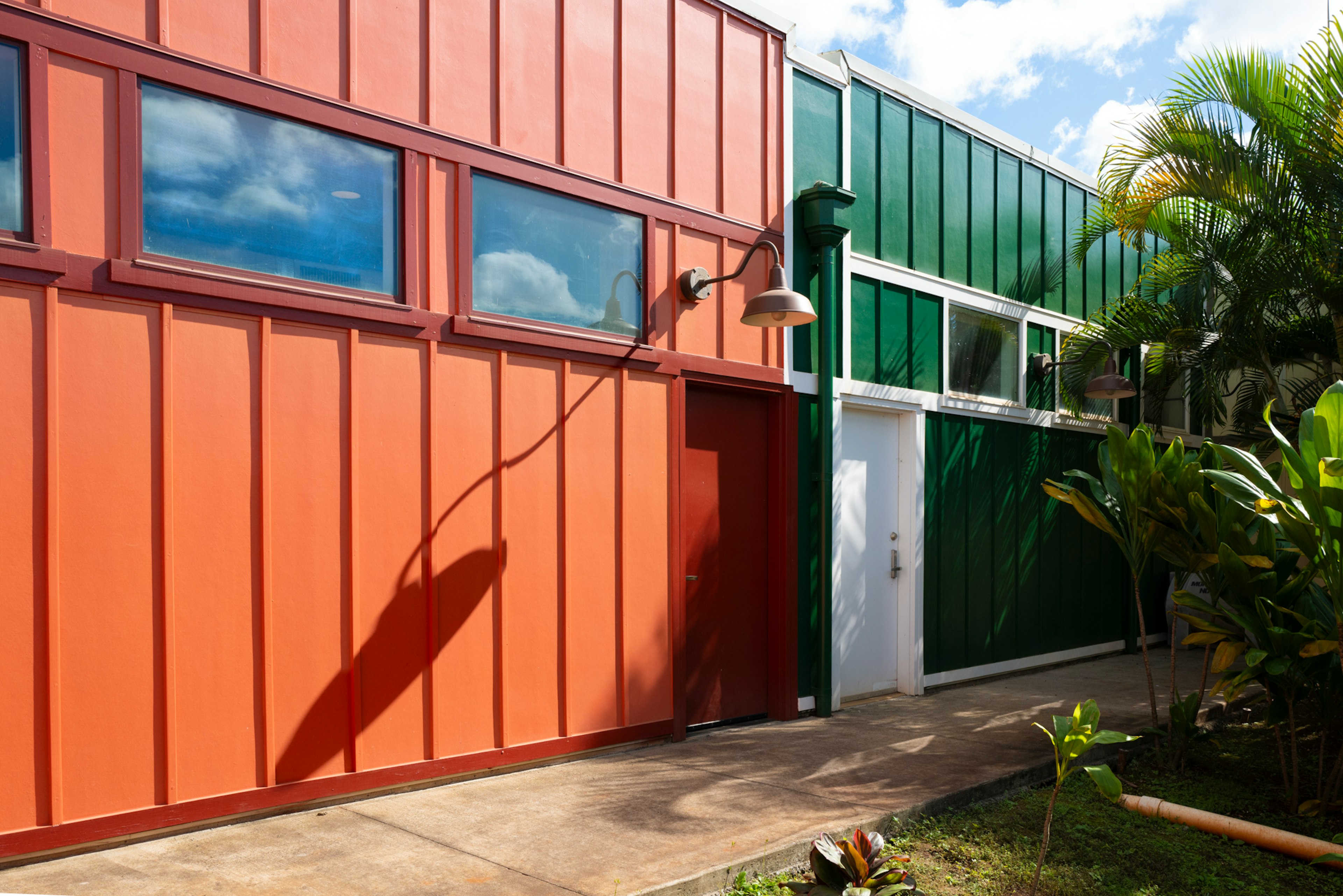 Modern building section with orange and green metal exterior and surrounding plants