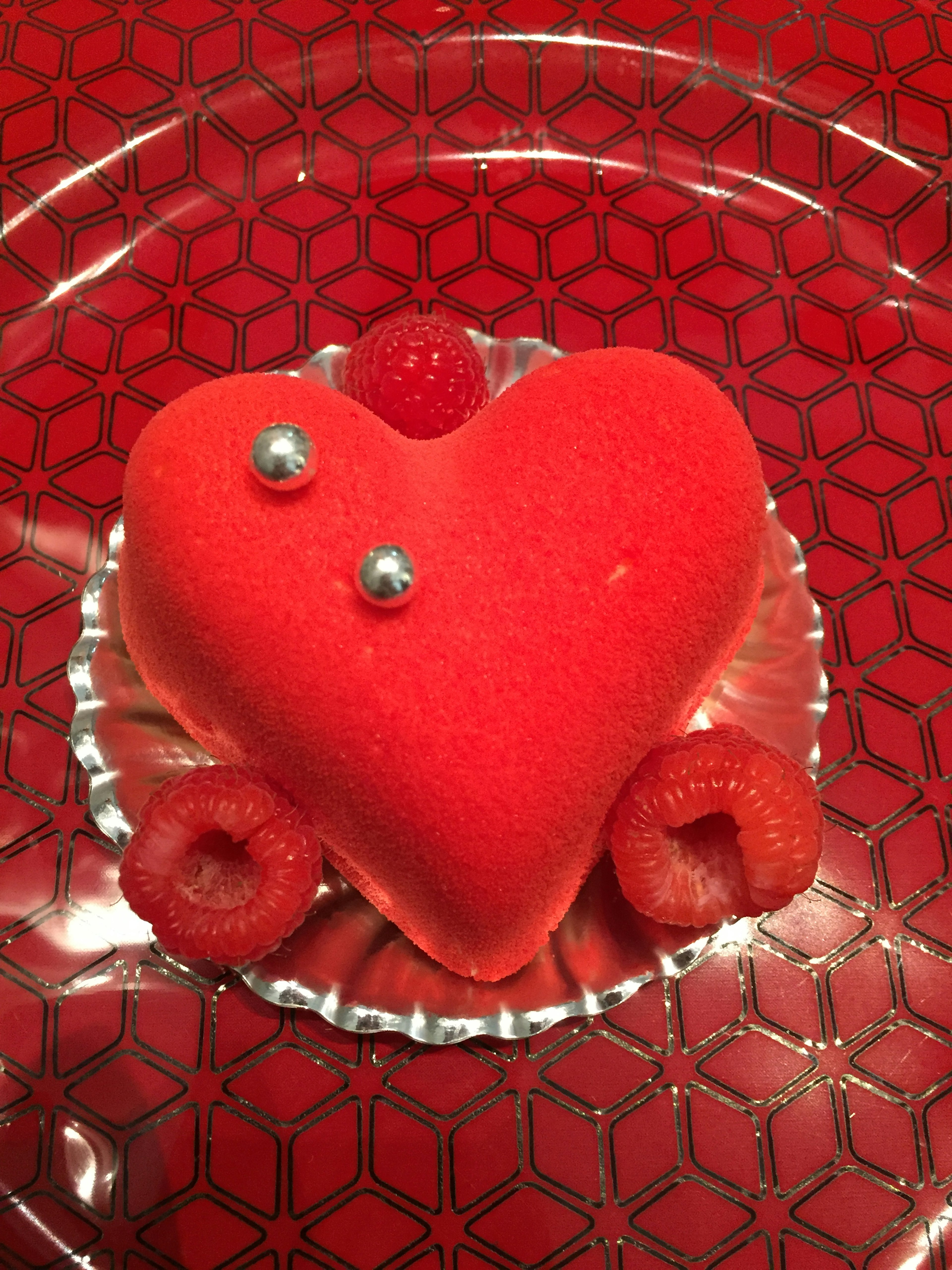 Red heart-shaped cake with raspberries and silver decorations