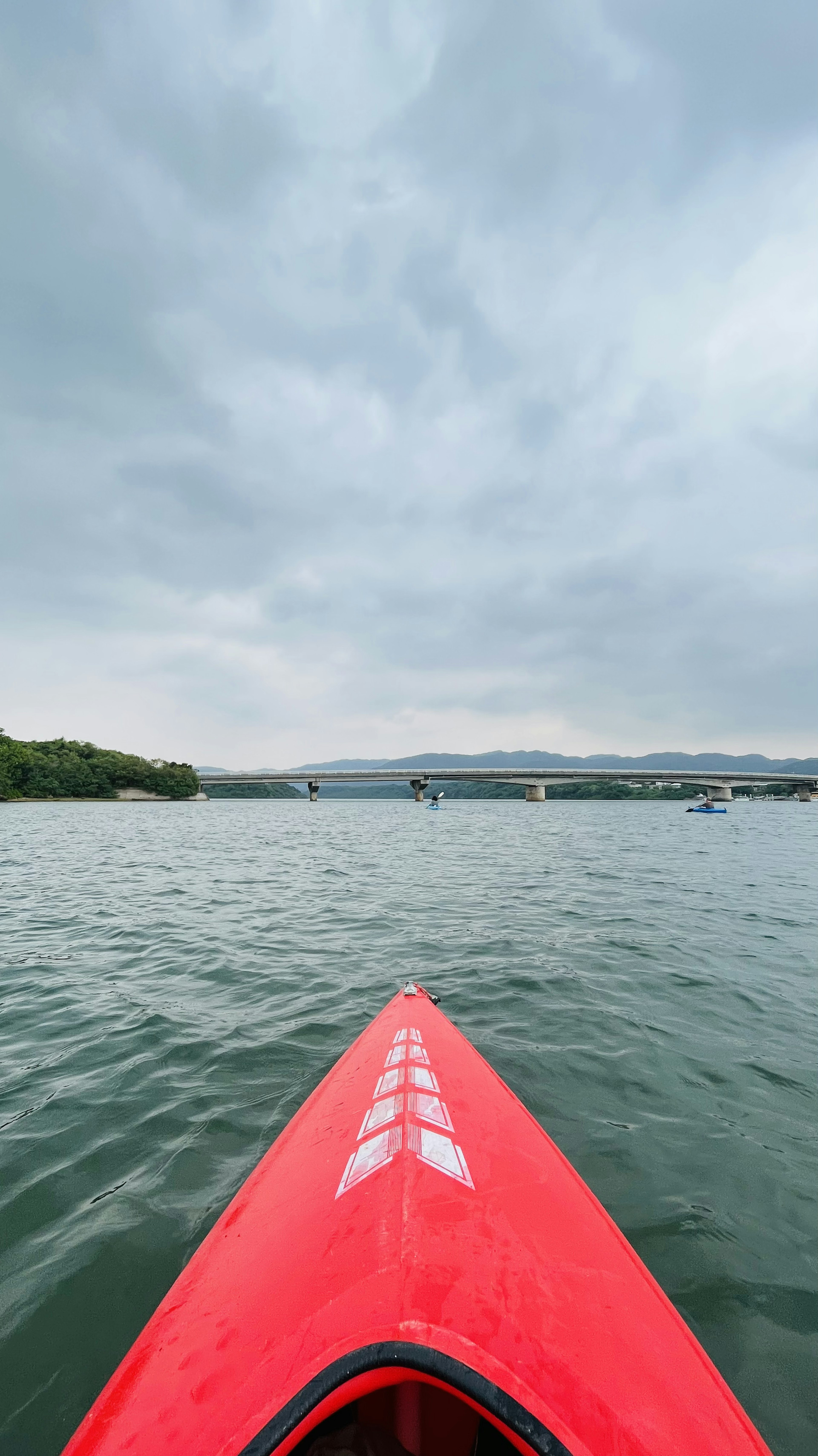 A red kayak's bow moving through the water under a cloudy sky