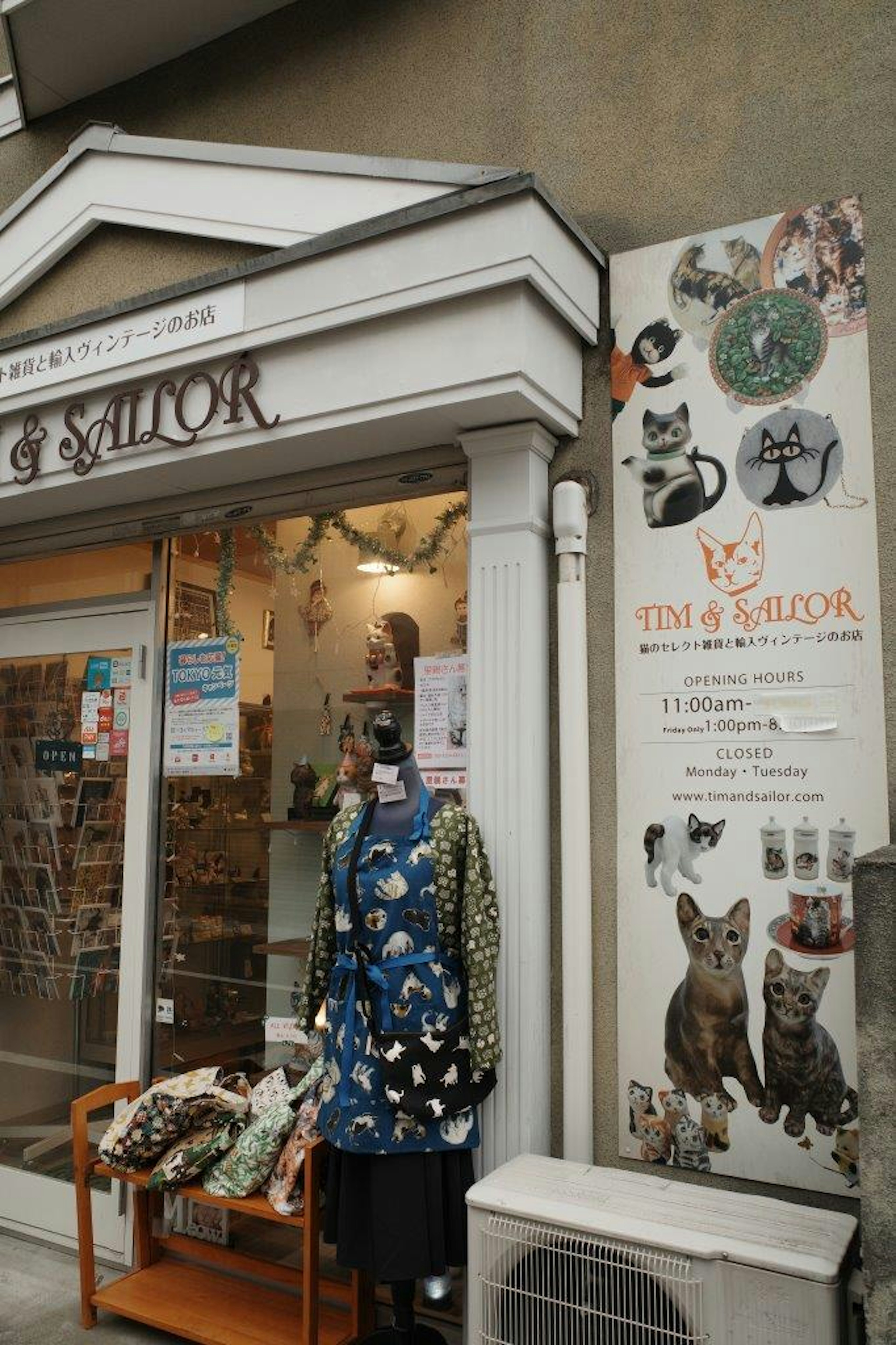 Un maniquí que lleva un delantal con temática de gatos está frente a una tienda