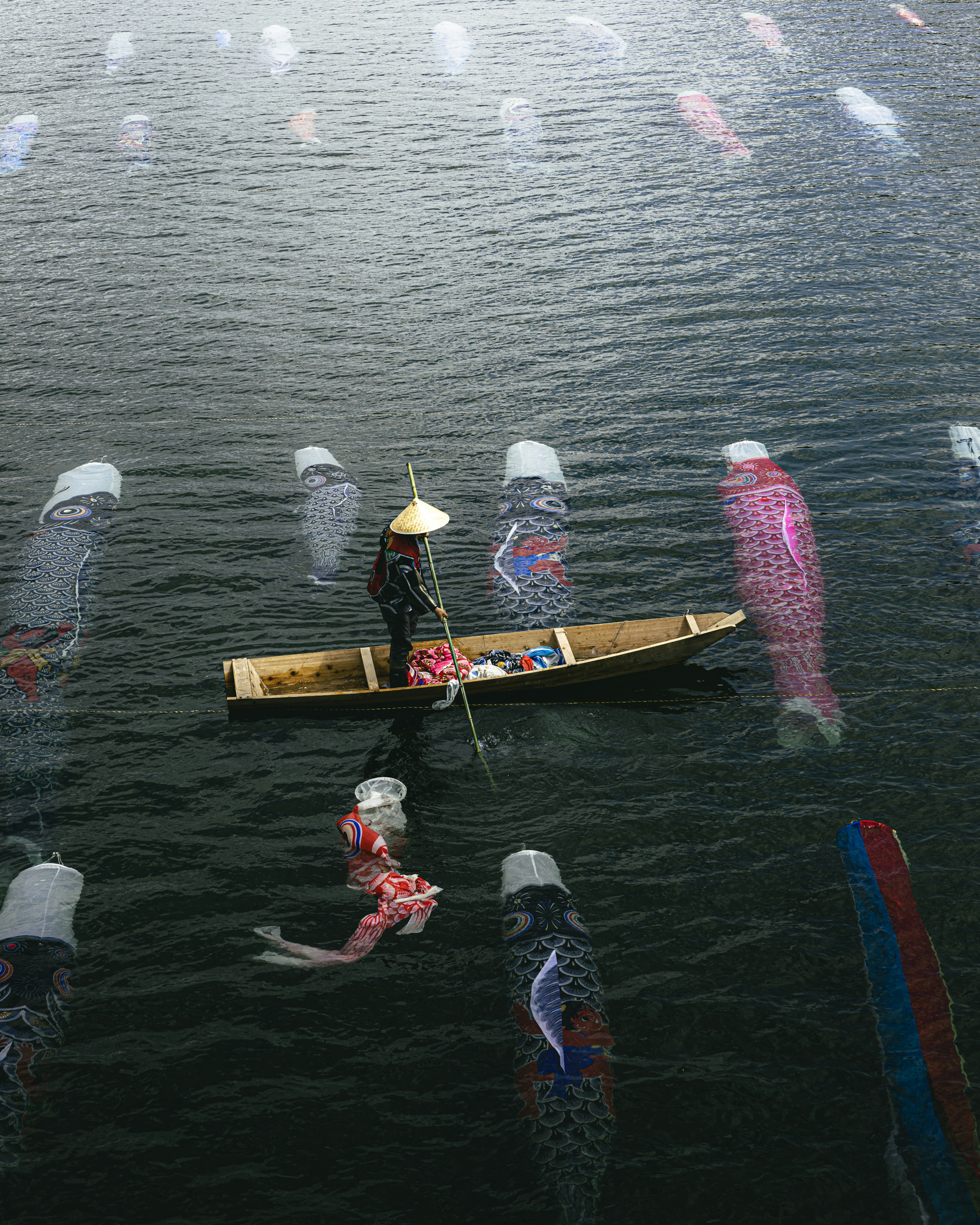 Une personne rame dans un bateau sur l'eau entourée de drapeaux en forme de poisson colorés