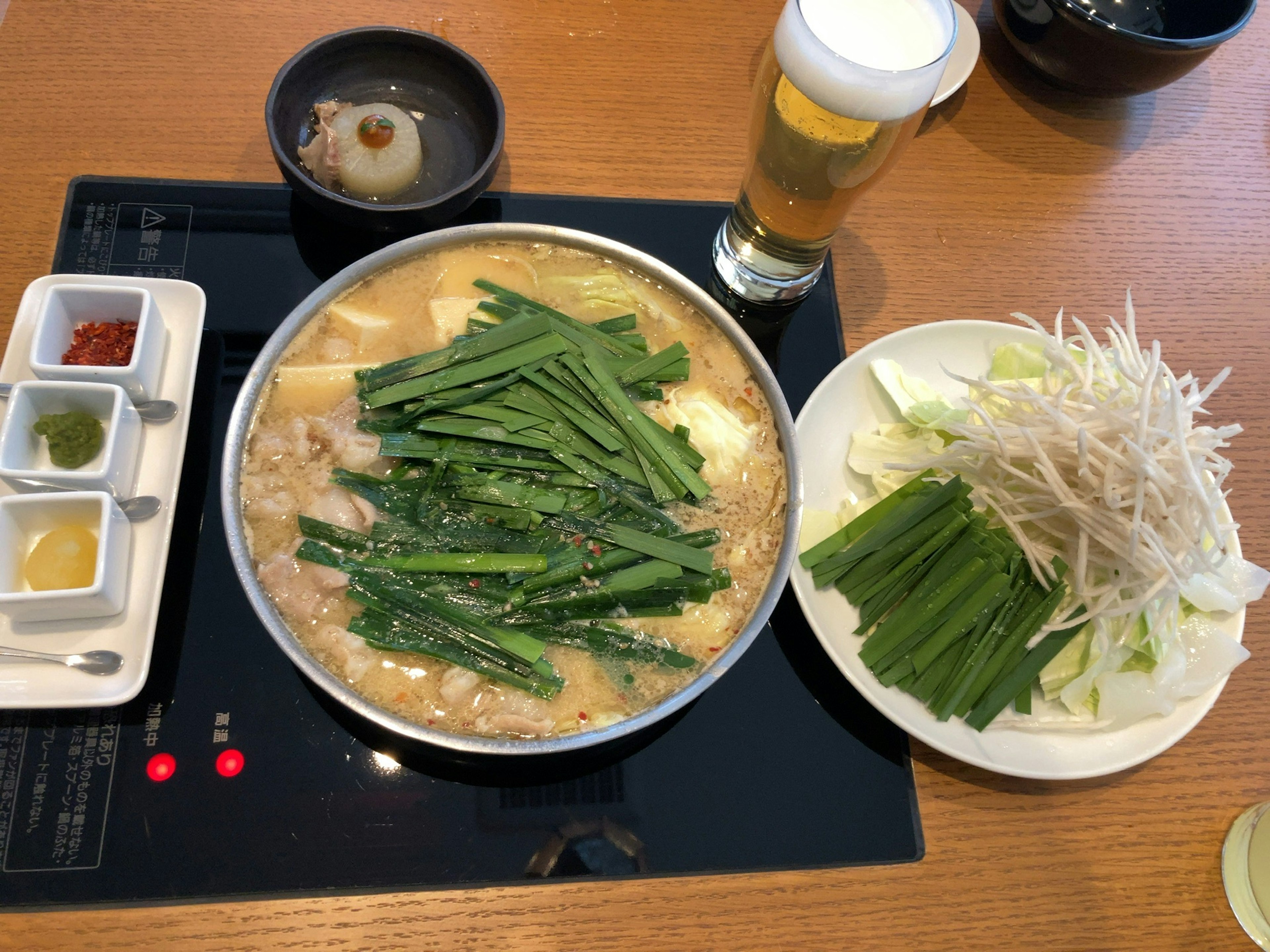 A hot pot dish topped with fresh green onions served with a side of cabbage and bean sprouts alongside a glass of beer