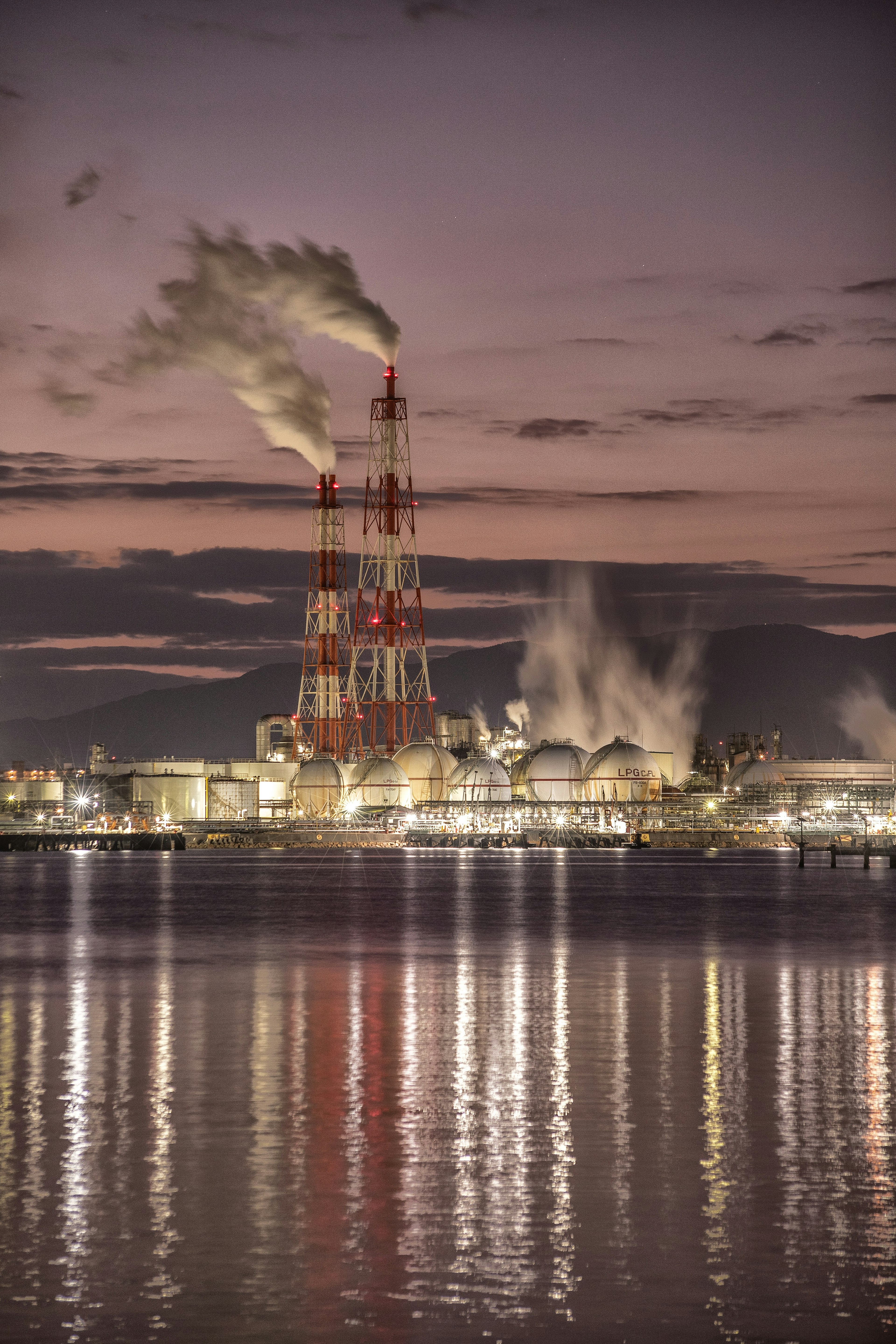 Factory smokestacks emitting smoke at dusk reflected in water