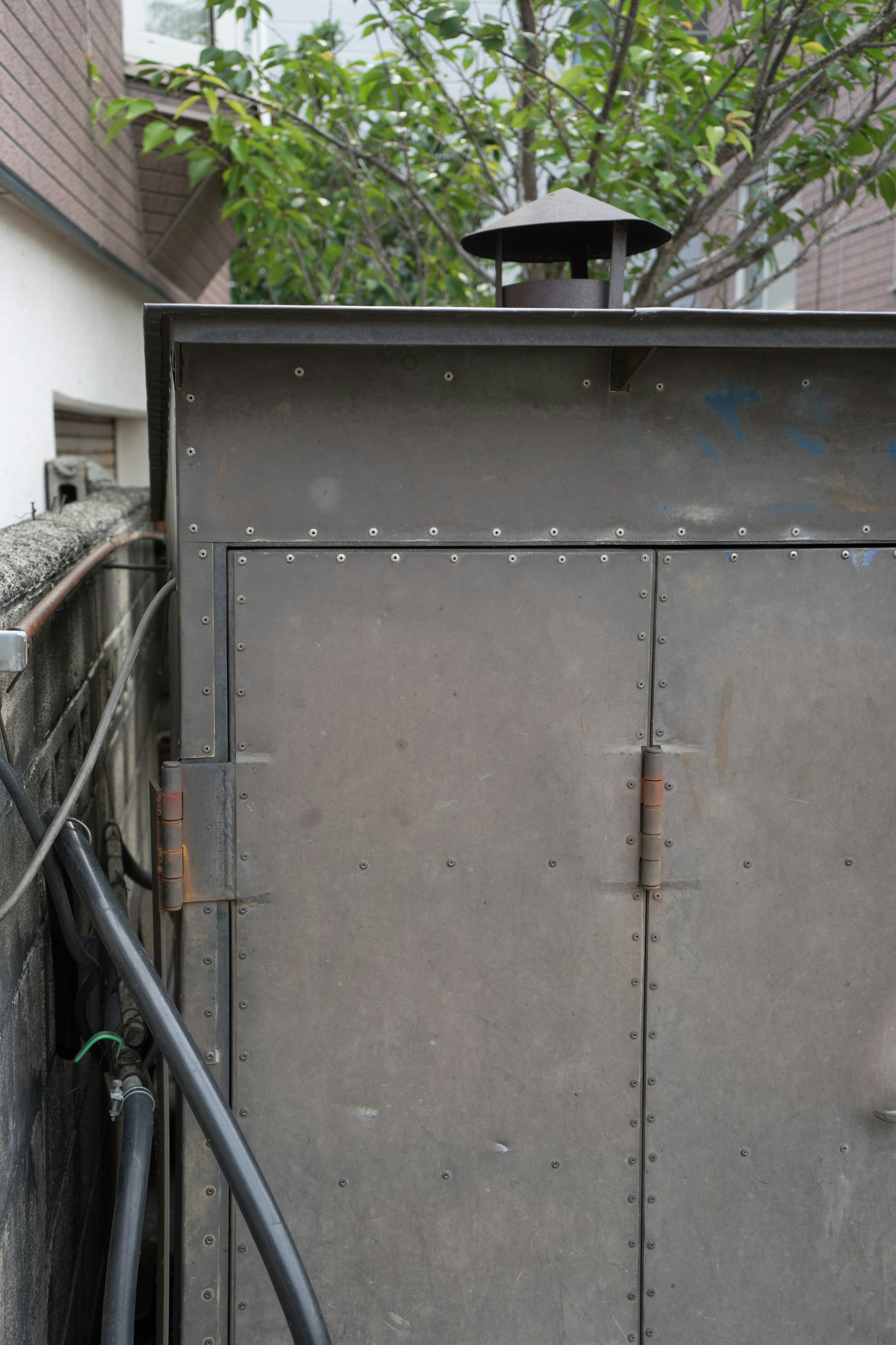 Image showing the back of a metal box with a chimney on top surrounded by green leaves