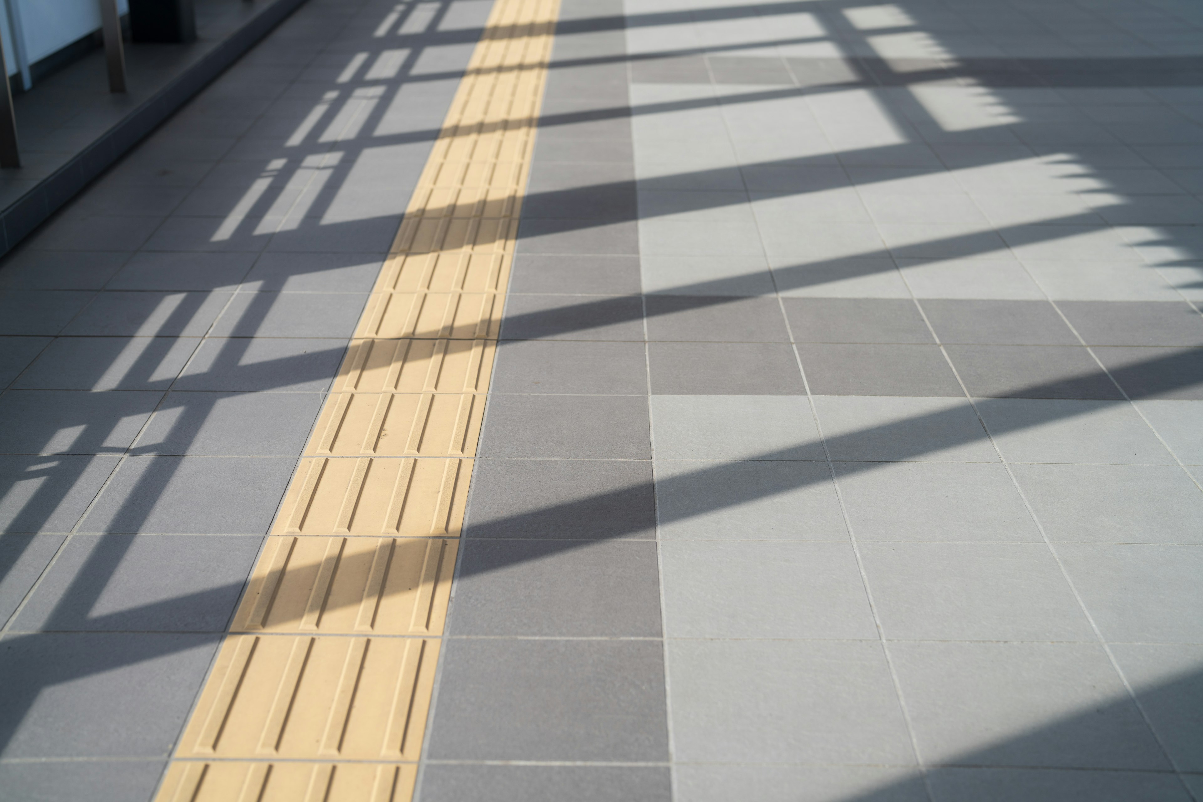 A walkway featuring a yellow tactile guide line on light-colored tiles with shadows