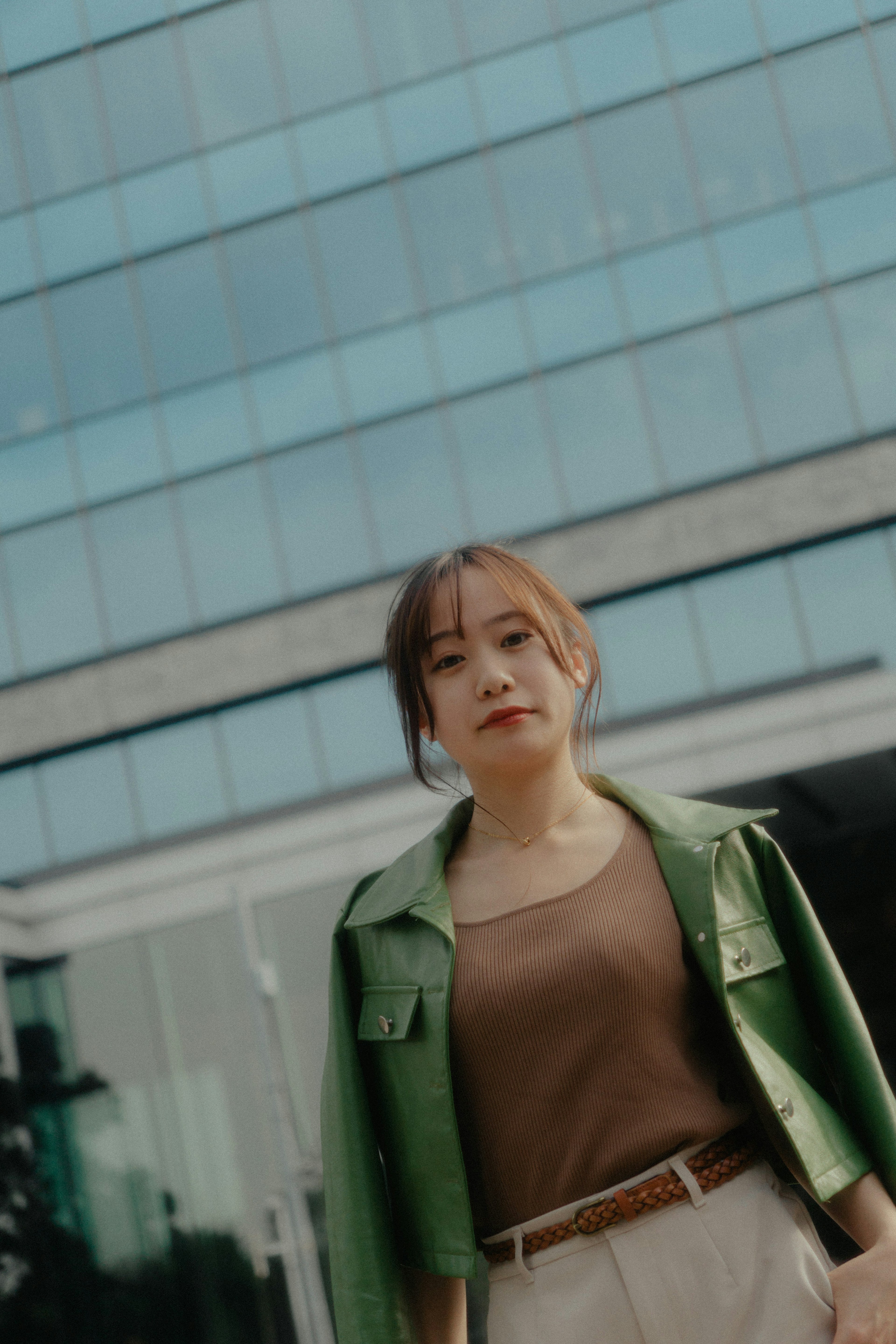 A woman in a green jacket stands in front of a modern building