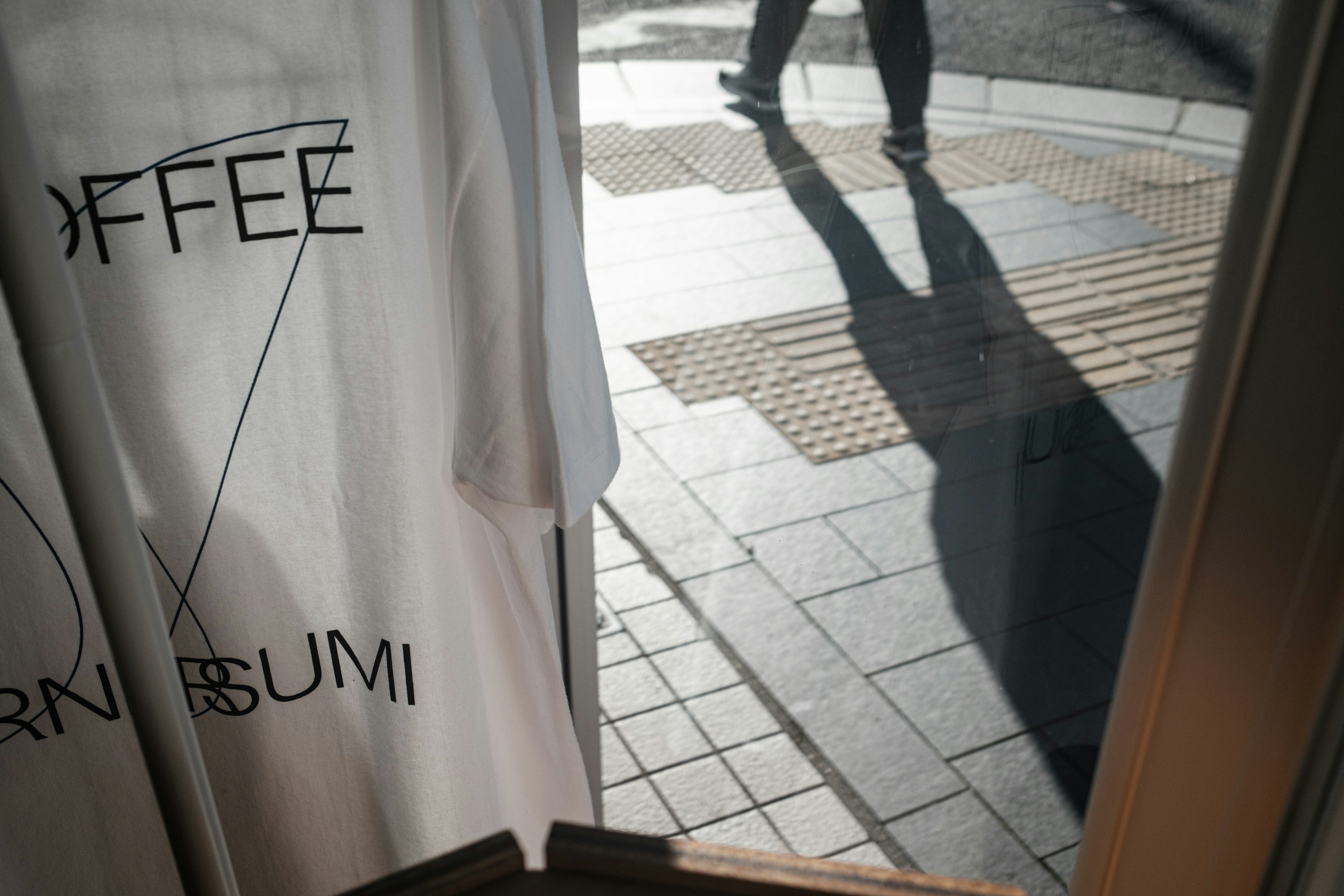 Schatten eines Fußgängers, der an einem Caféfenster mit einem weißen Vorhang mit Kaffeebranding vorbeigeht