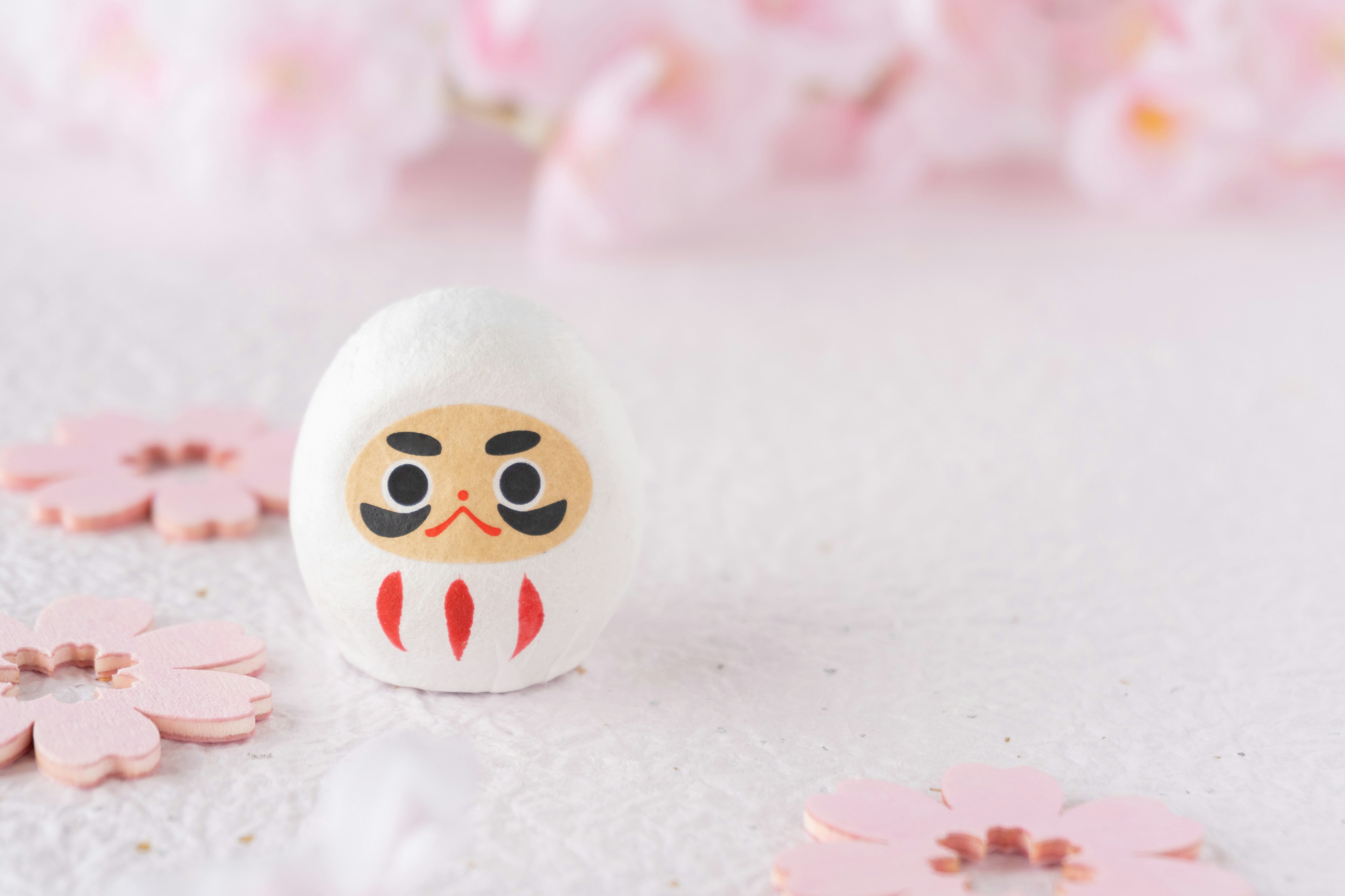 Une poupée Daruma blanche placée sur des pétales de cerisier roses