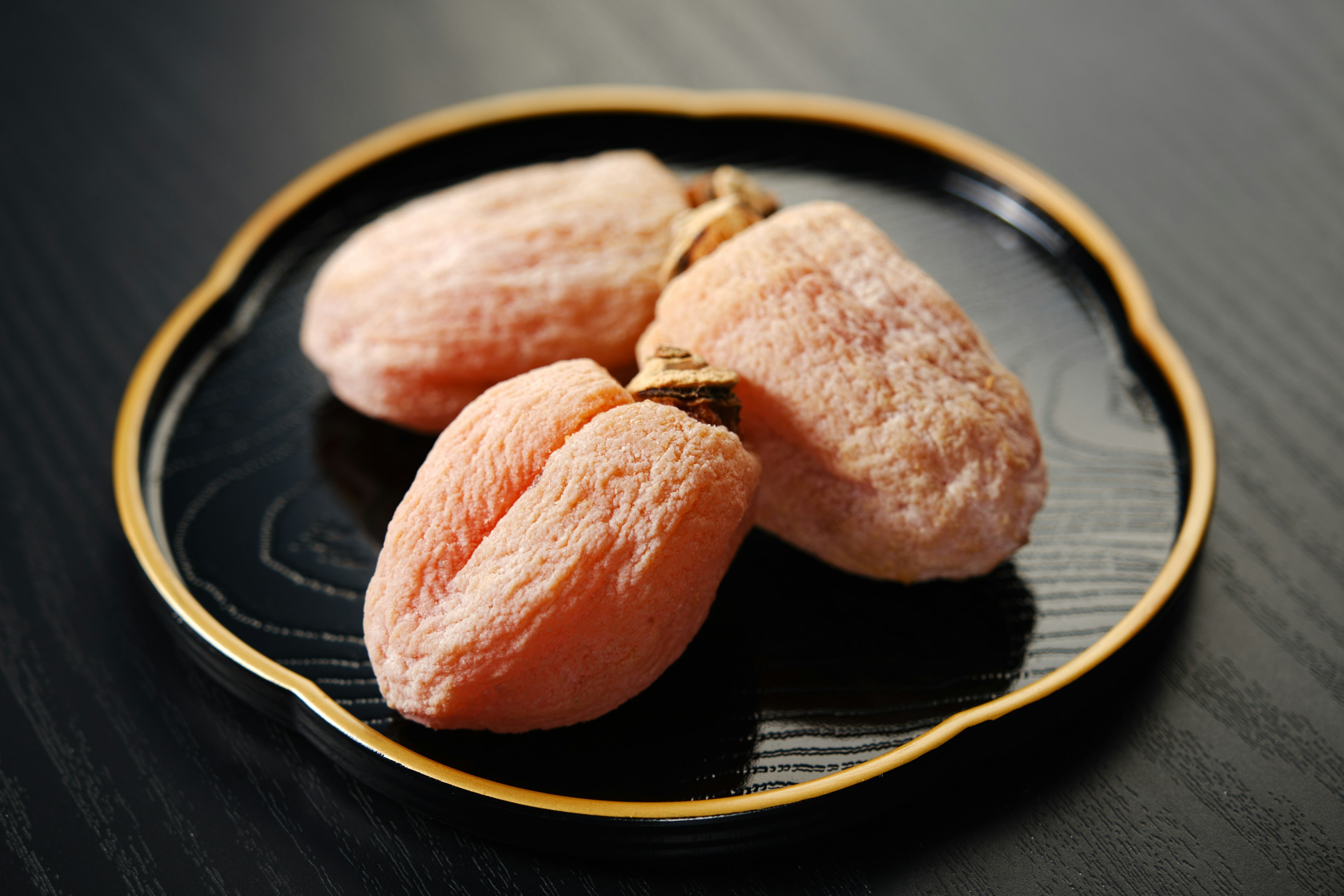 Trois bonbons en forme de fruits roses sur une assiette noire