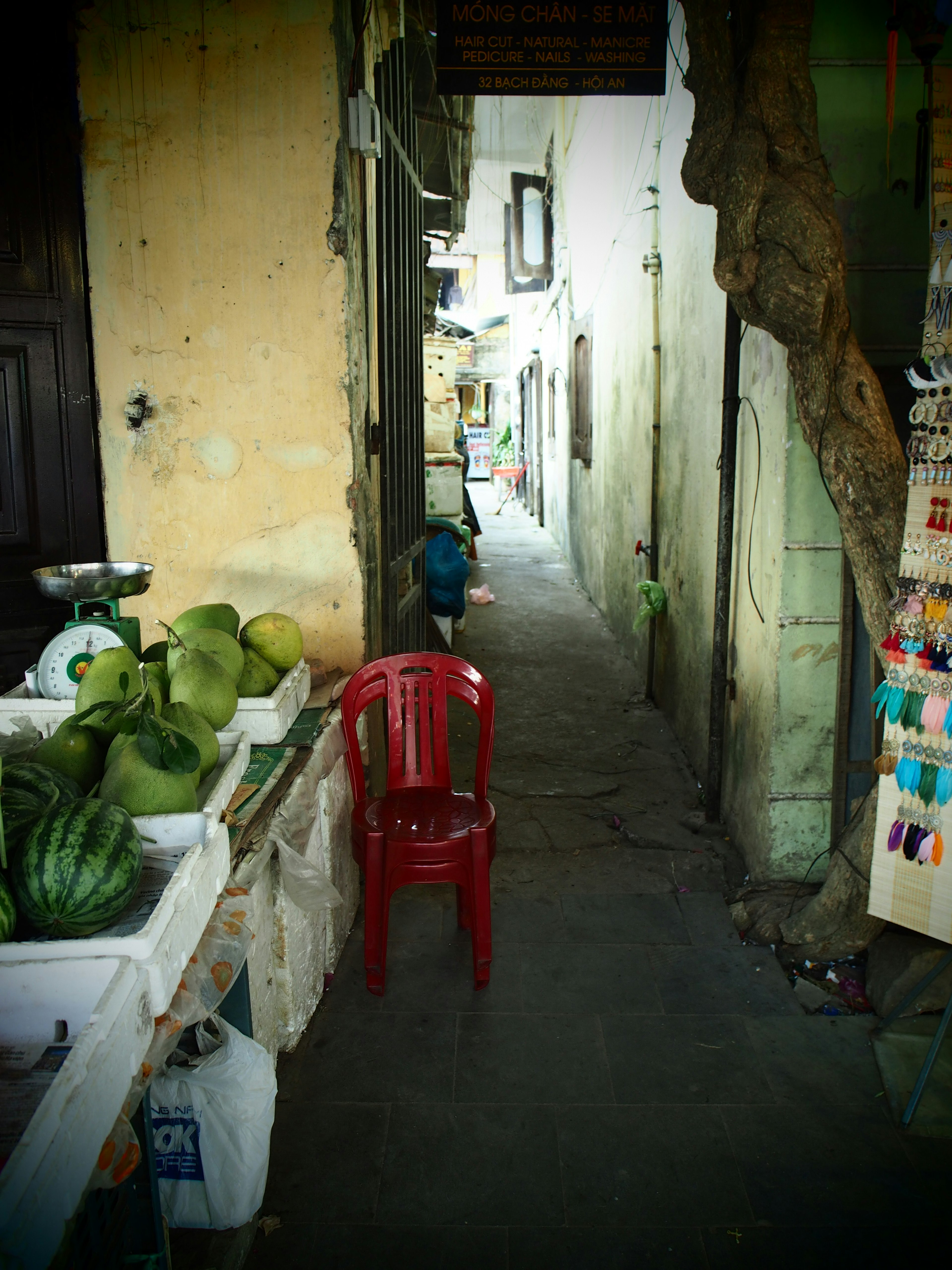 Allée étroite avec une chaise rouge et un stand de fruits