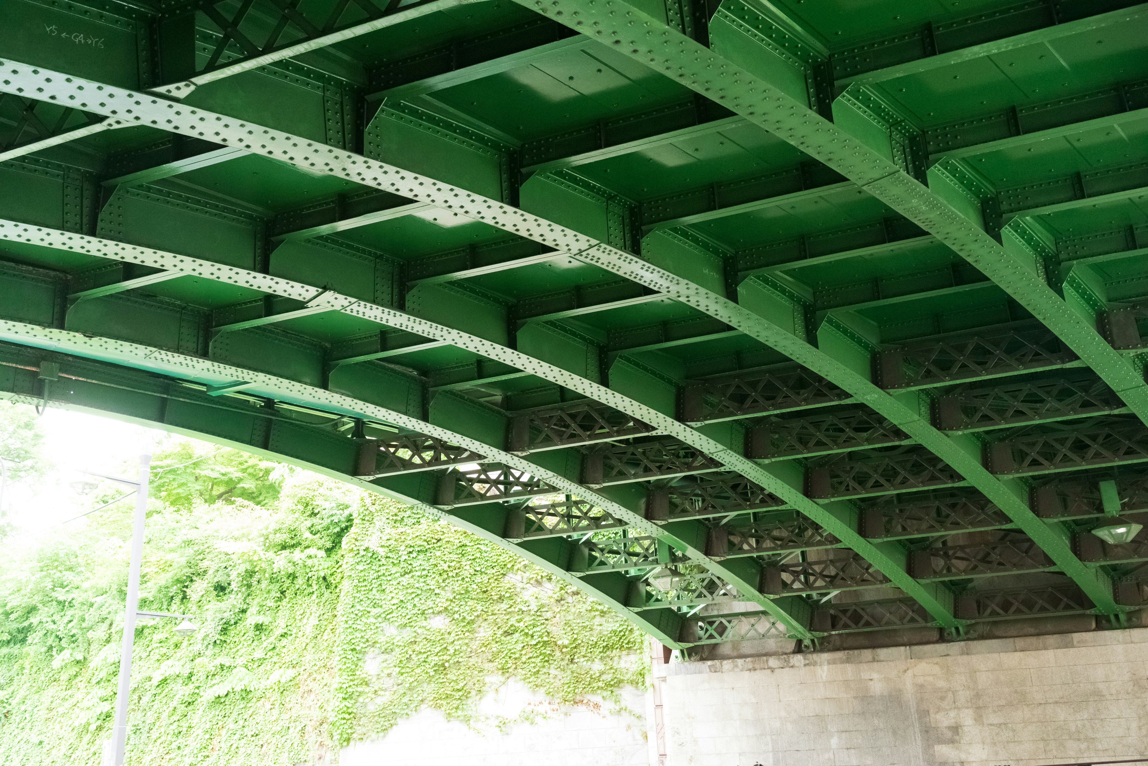 Gambar menunjukkan bagian bawah struktur jembatan melengkung hijau