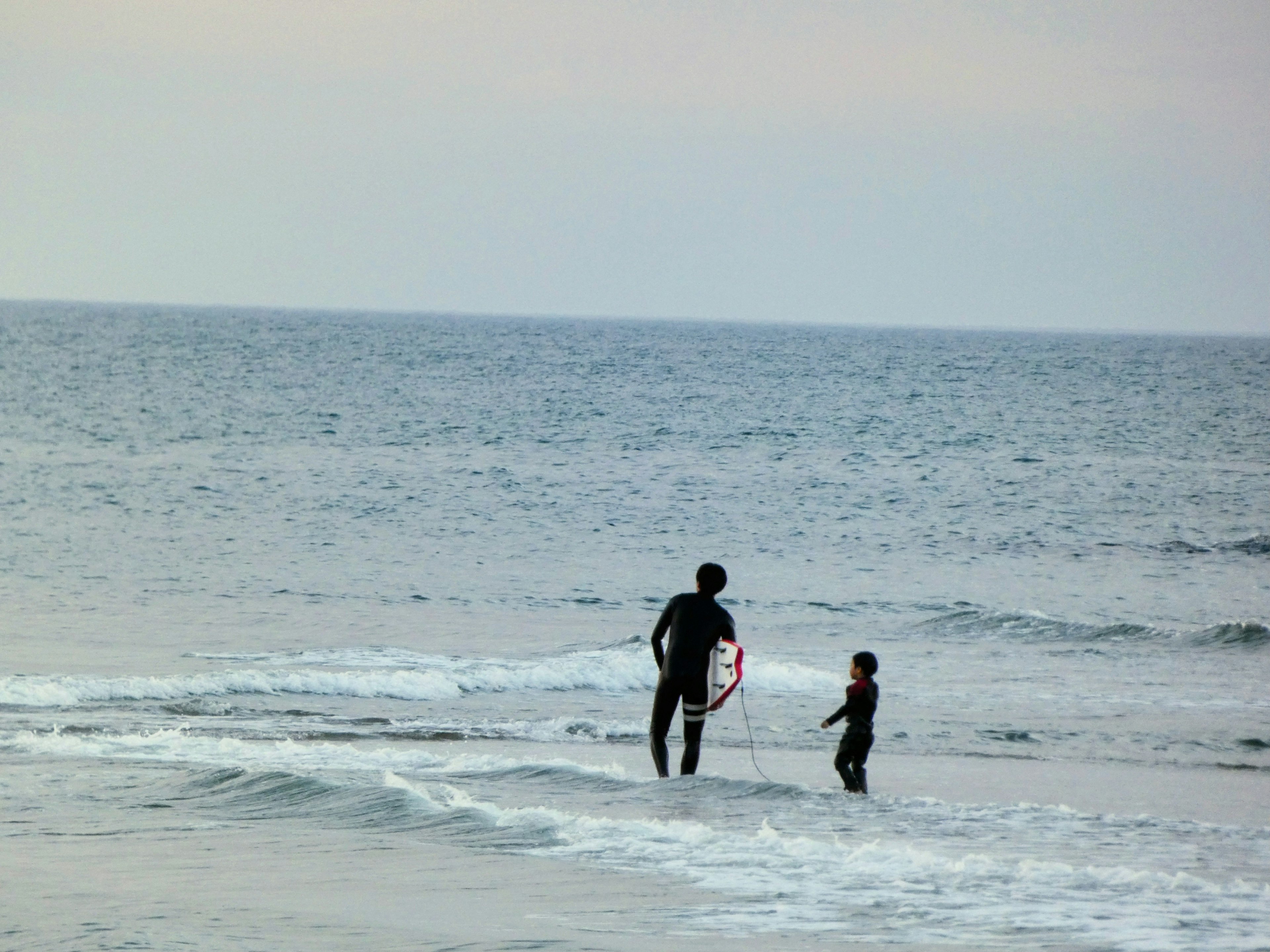 Siluet orang dewasa dengan papan selancar dan anak di pantai