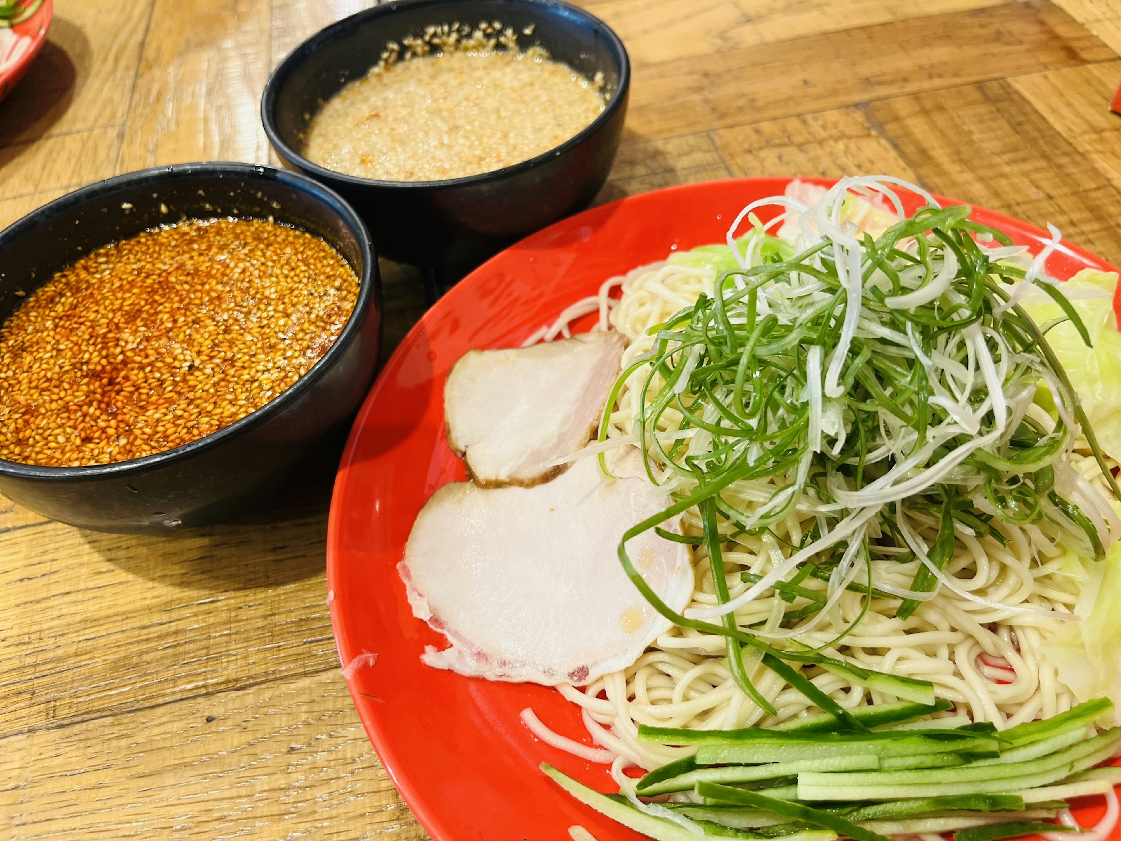 Cold noodles served on a red plate with green onions and slices of pork