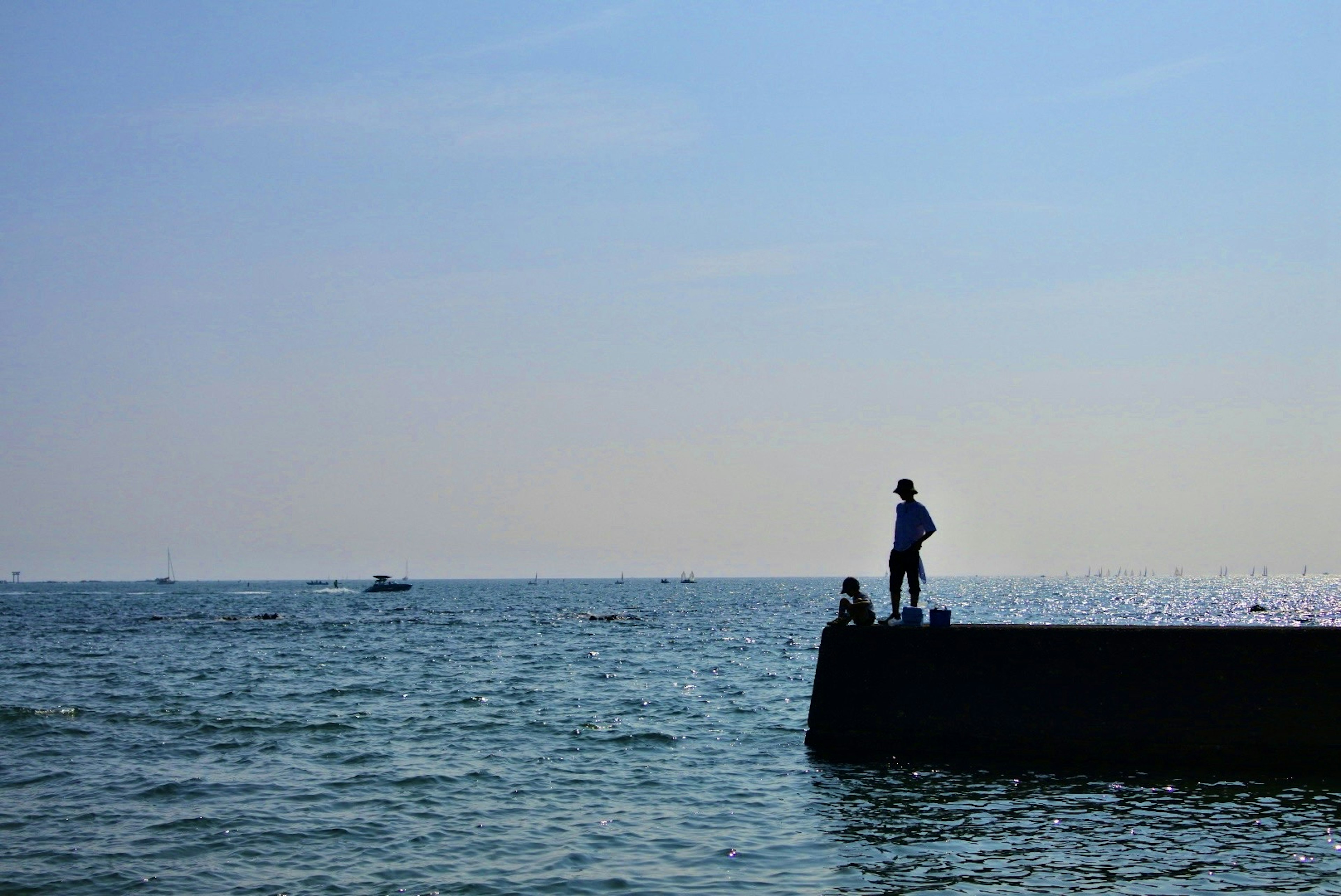 Silhouette of a person standing on a pier against a blue sea and sky