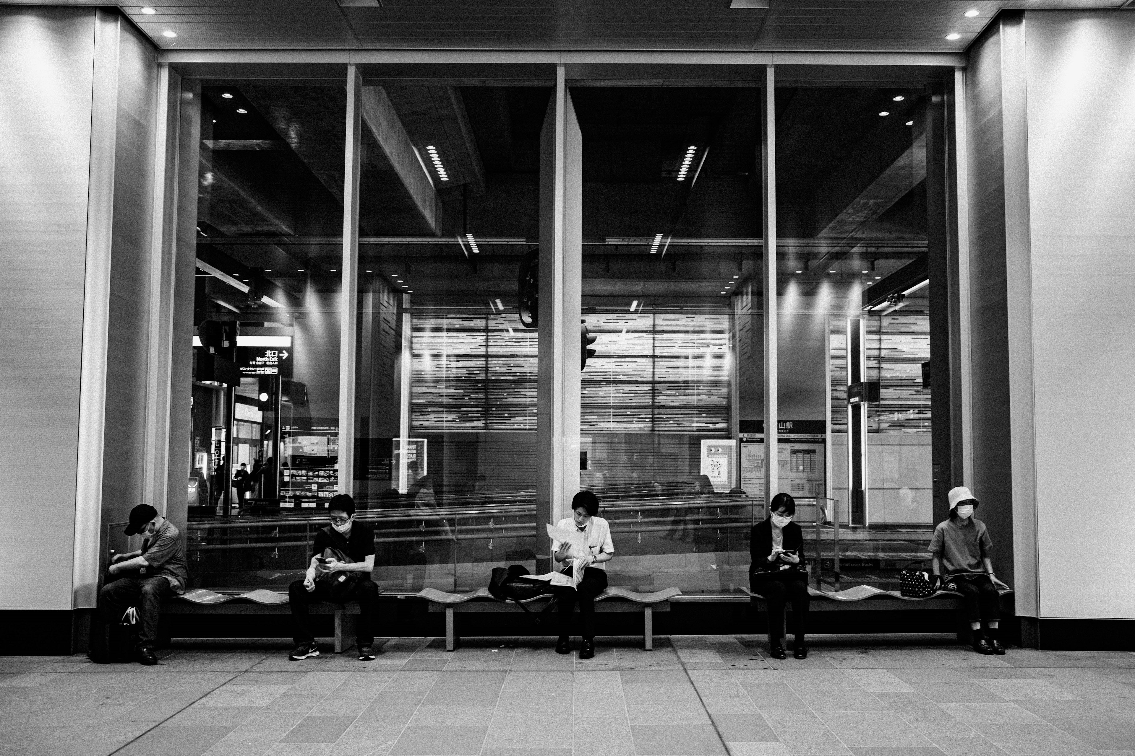 Black and white photo of people sitting in a train station waiting area