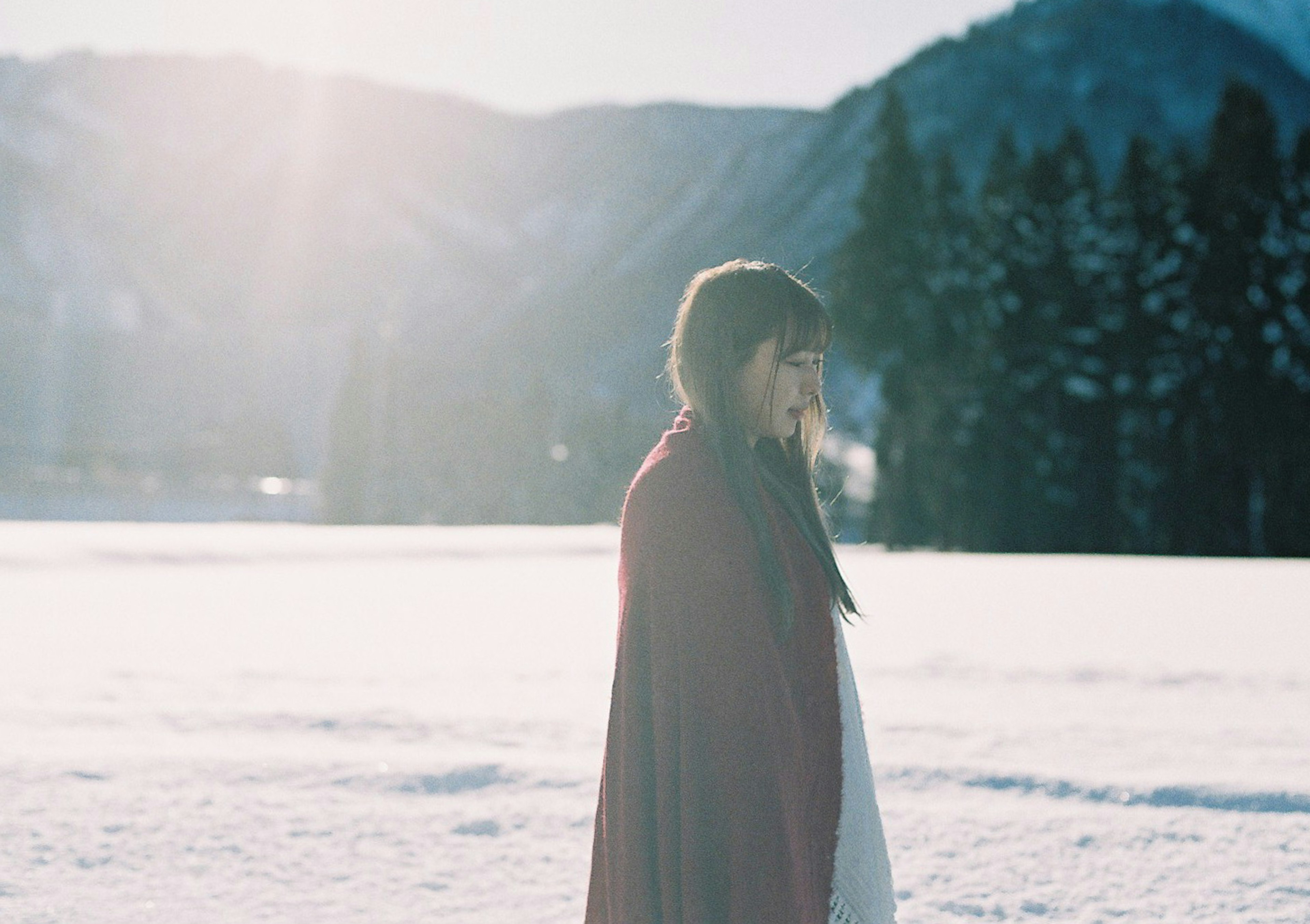 Femme marchant dans la neige vêtue d'une cape rouge montagnes et arbres en arrière-plan