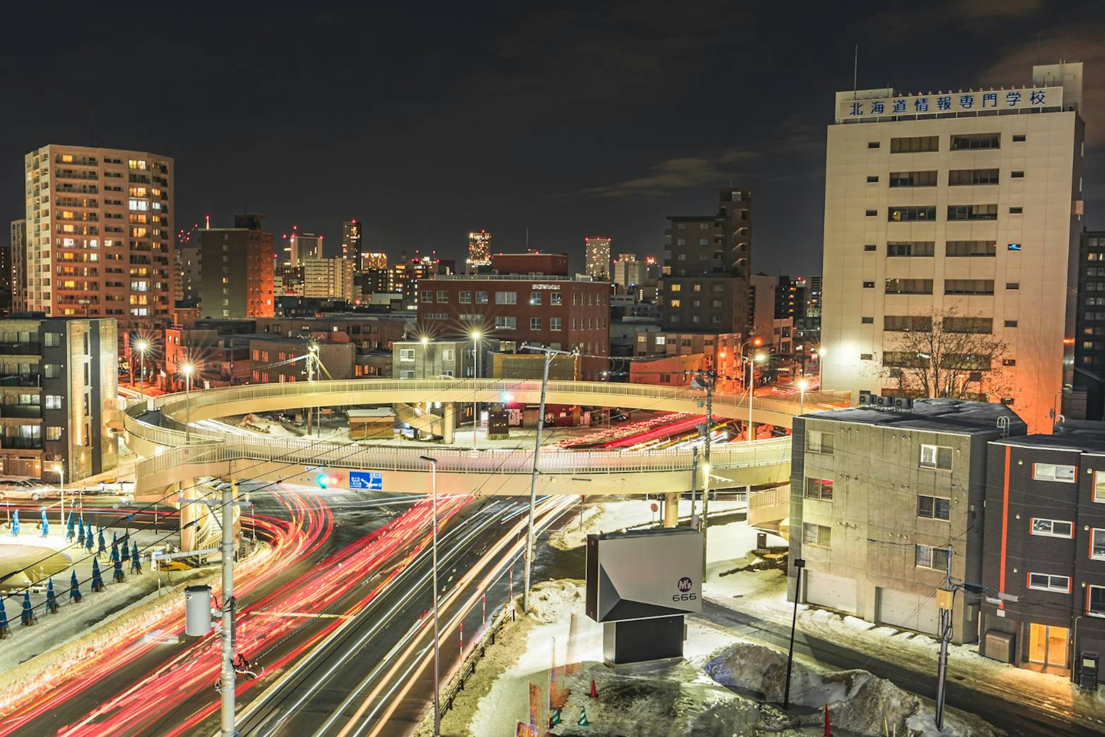 Paesaggio urbano notturno con edifici illuminati e un'autostrada con traffico scorrevole