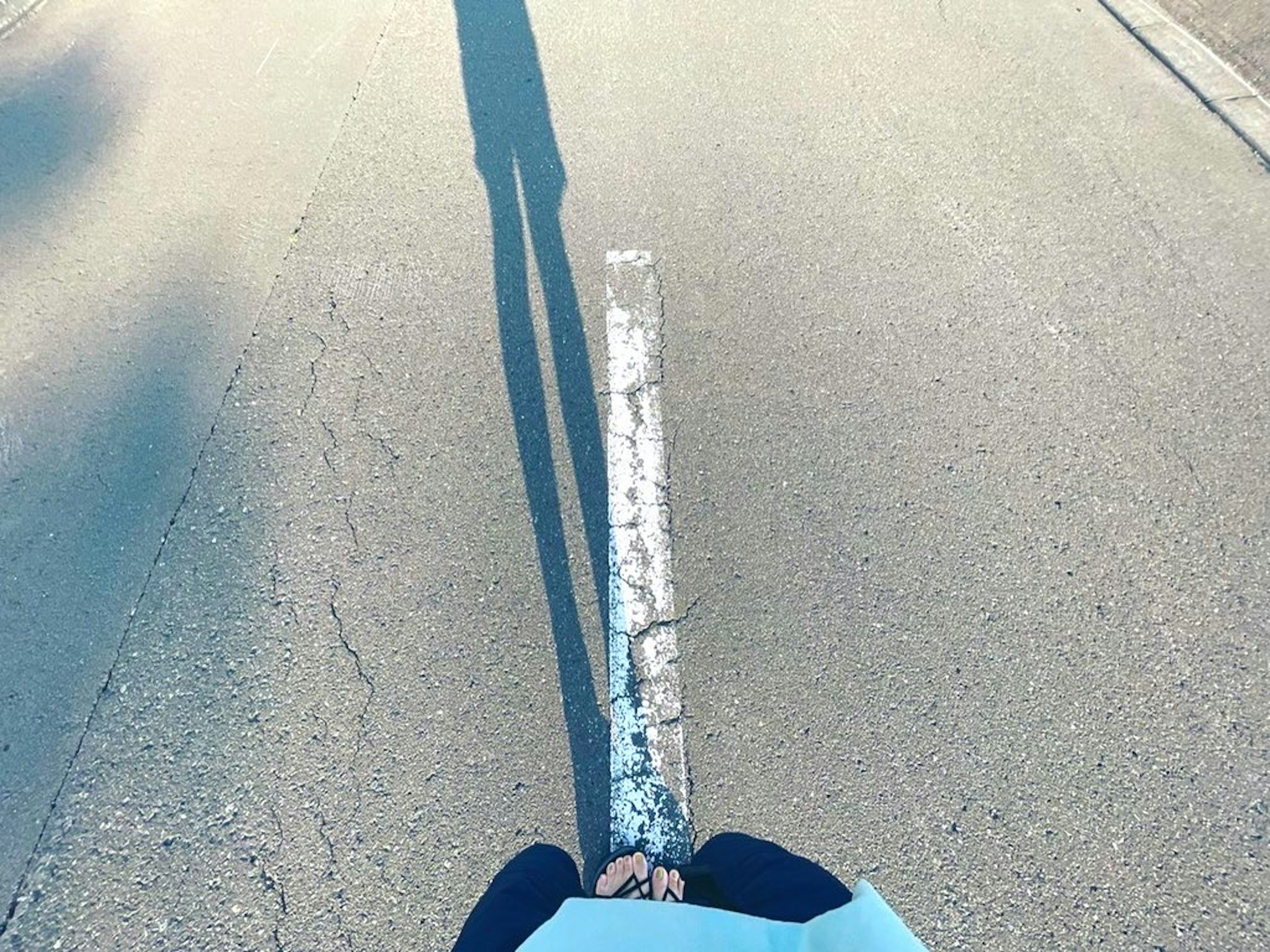 Bild zeigt eine Person in einem blauen Shirt, die in der Mitte der Straße steht und einen langen Schatten wirft