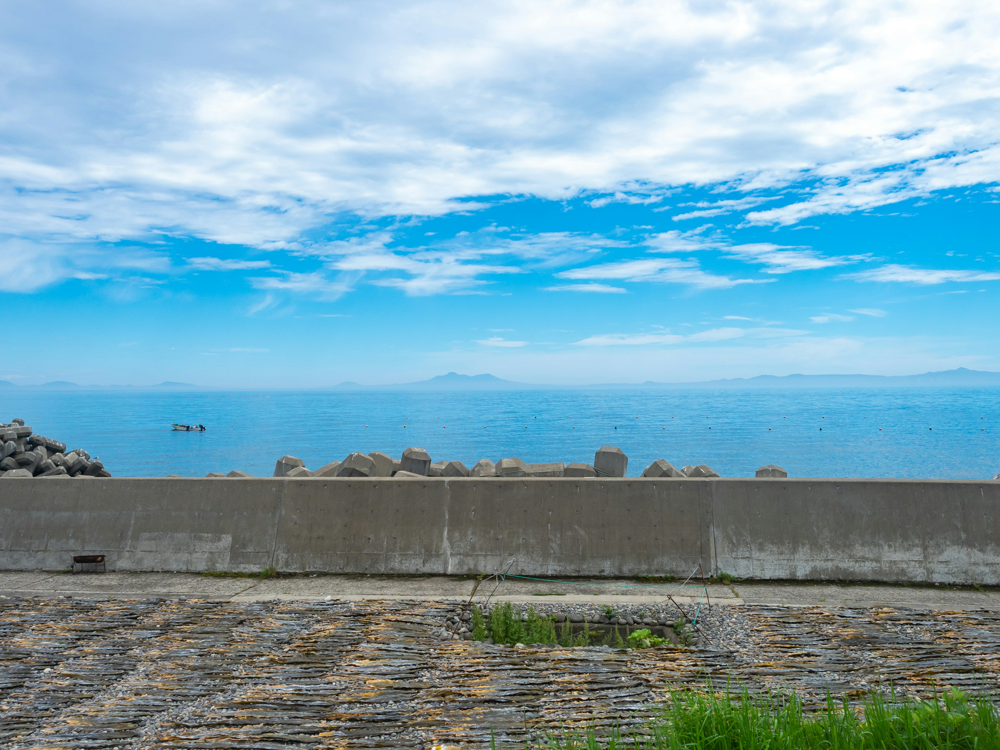 Vista panoramica dell'oceano blu e del cielo nuvoloso con una barriera di pietra e pavimentazione