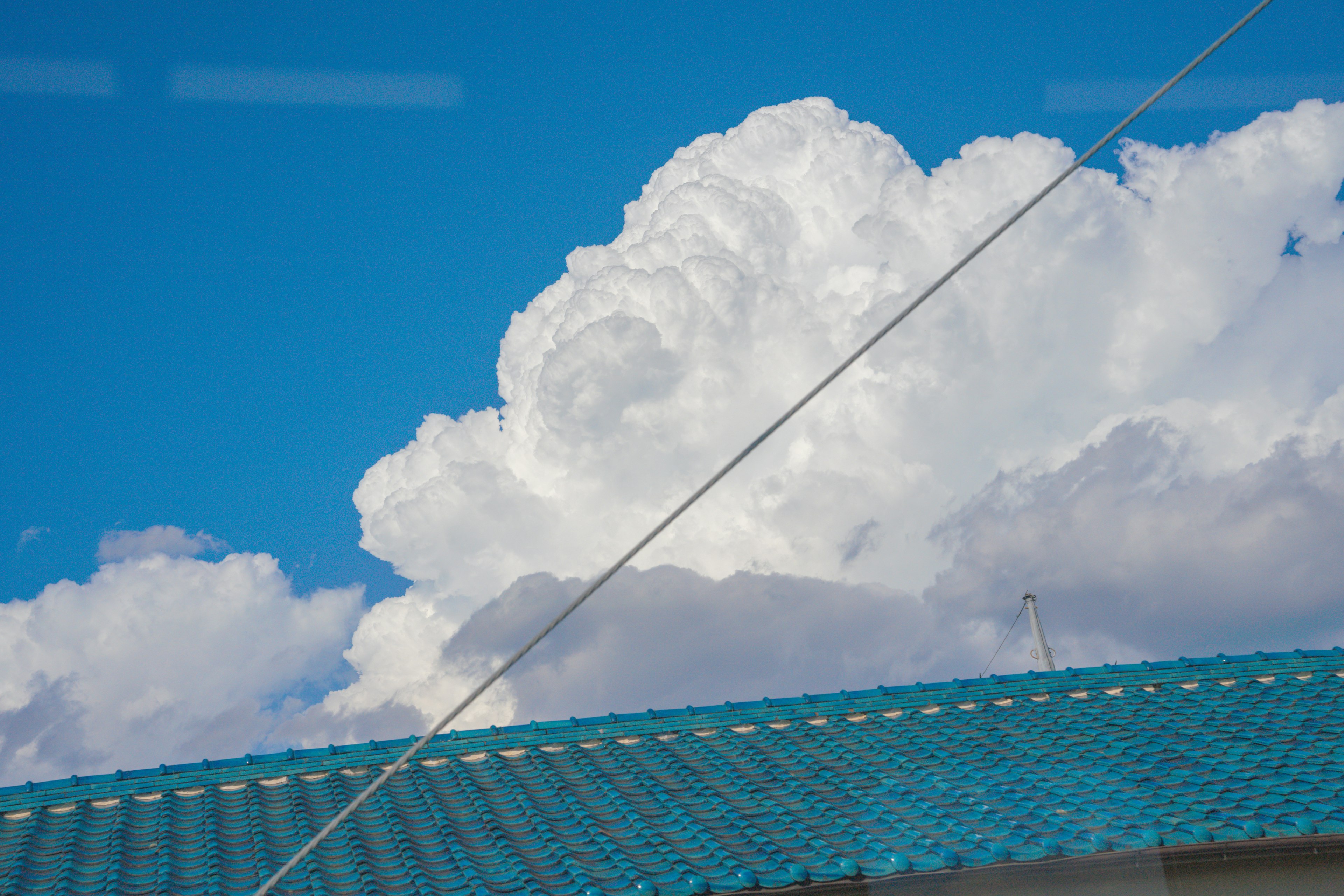 青空にふわふわした白い雲と青い屋根