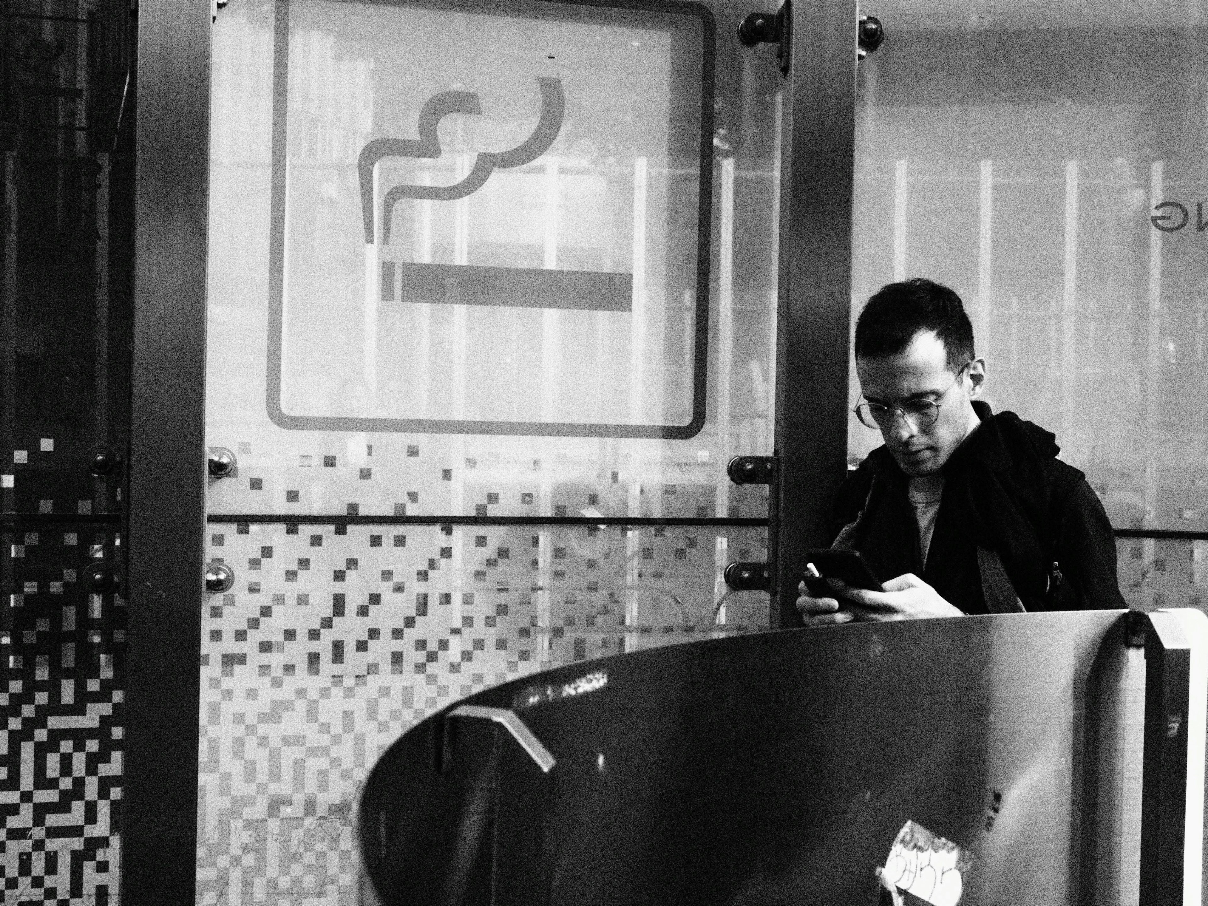 A man using a smartphone inside a smoking area in black and white