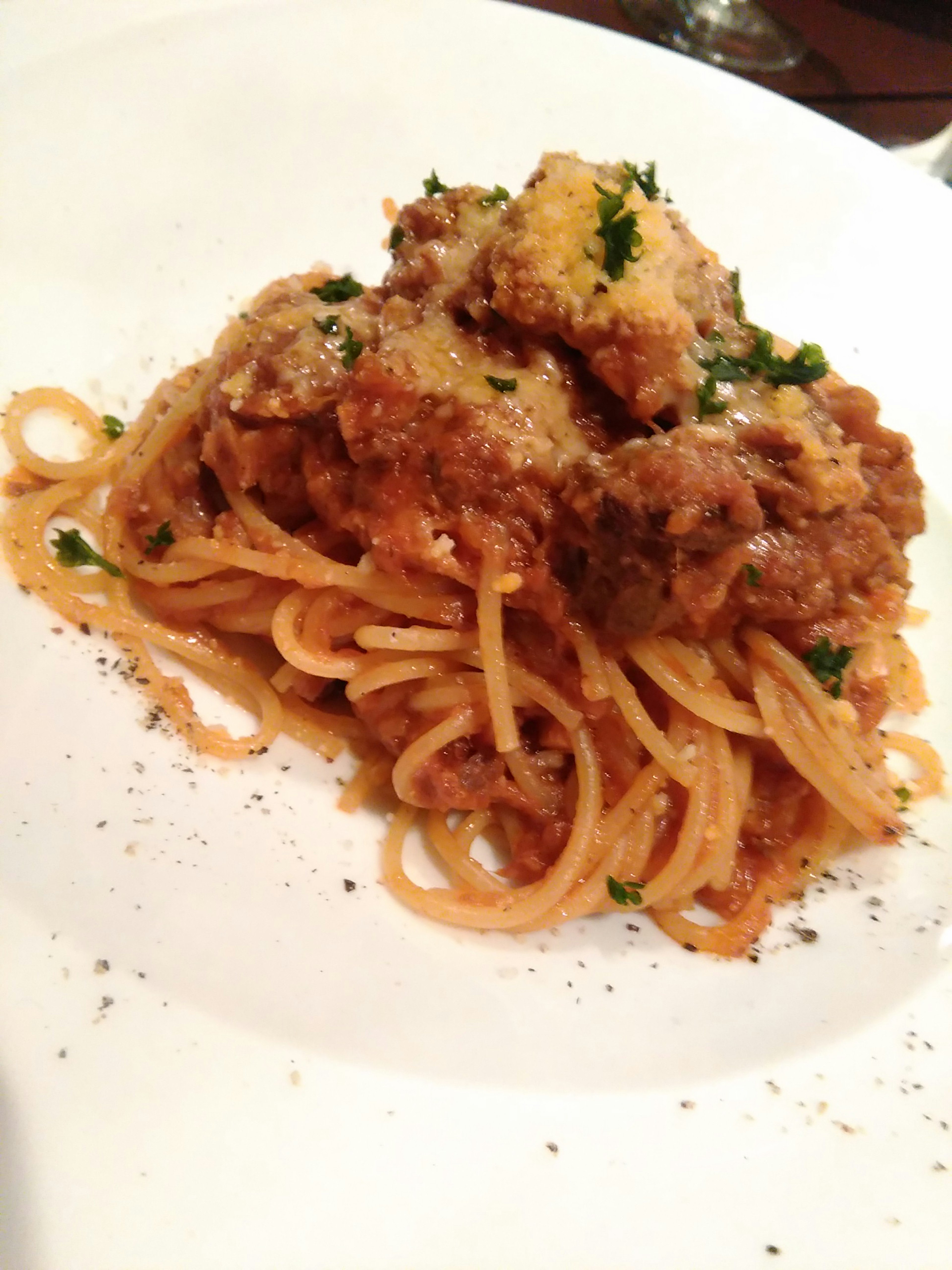 Plate of spaghetti topped with meat sauce parmesan cheese and parsley