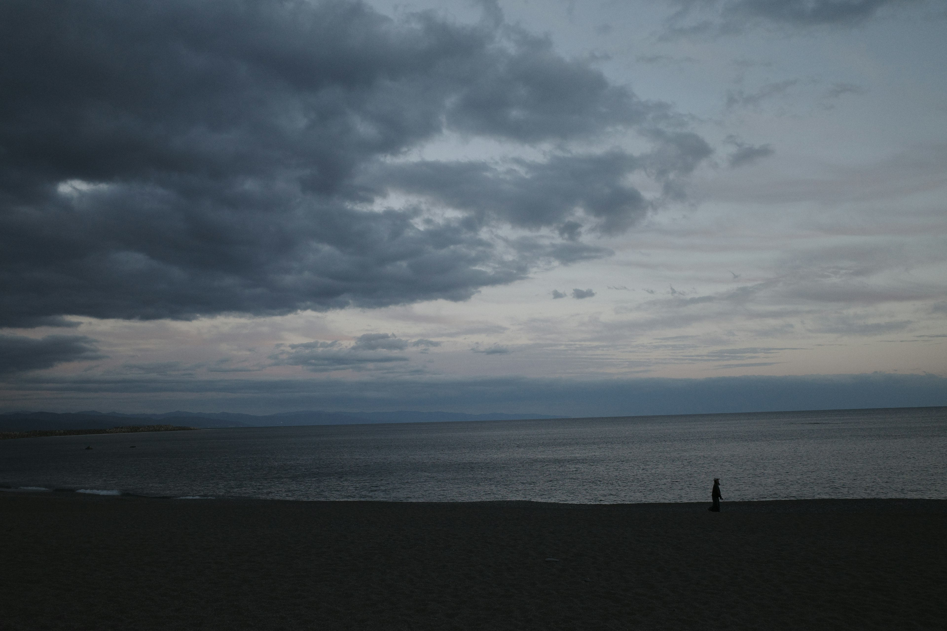 暗い雲が広がる海岸線を見つめる人物のシルエット