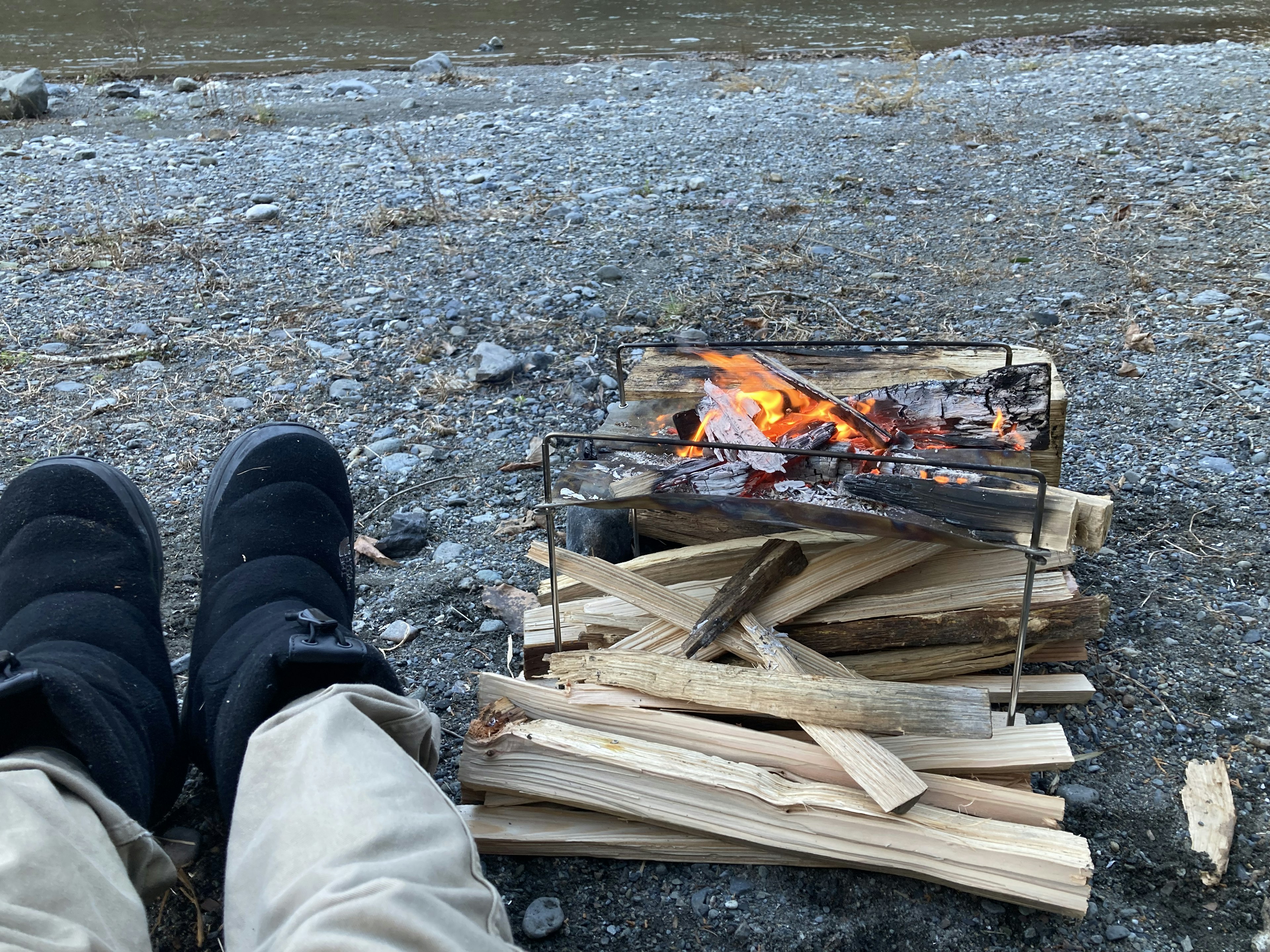 Füße einer Person vor einem Lagerfeuer mit einem Holzstapel