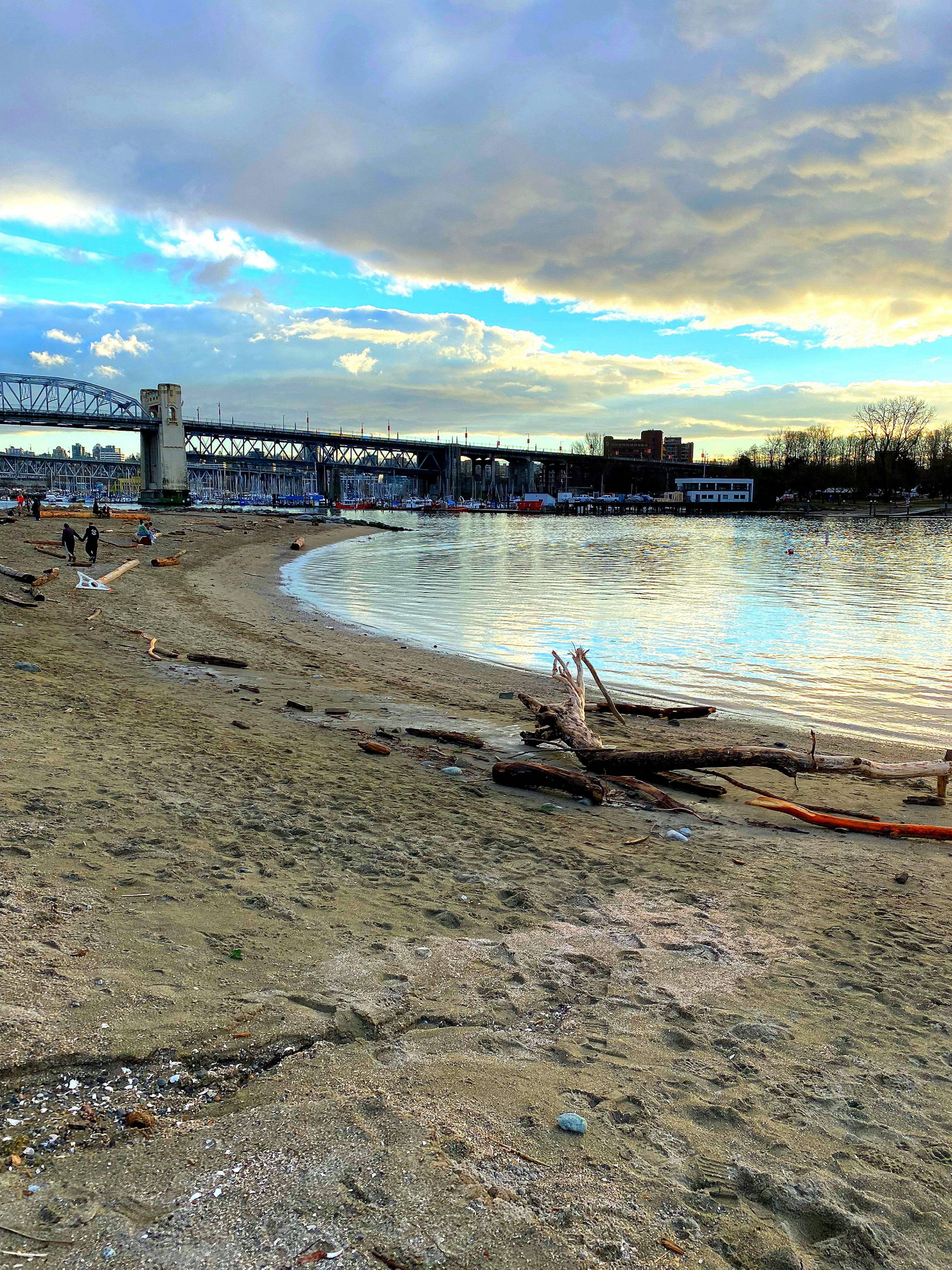 Pemandangan pantai yang tenang dengan langit biru dan gelombang lembut Jembatan dan bangunan terlihat di kejauhan