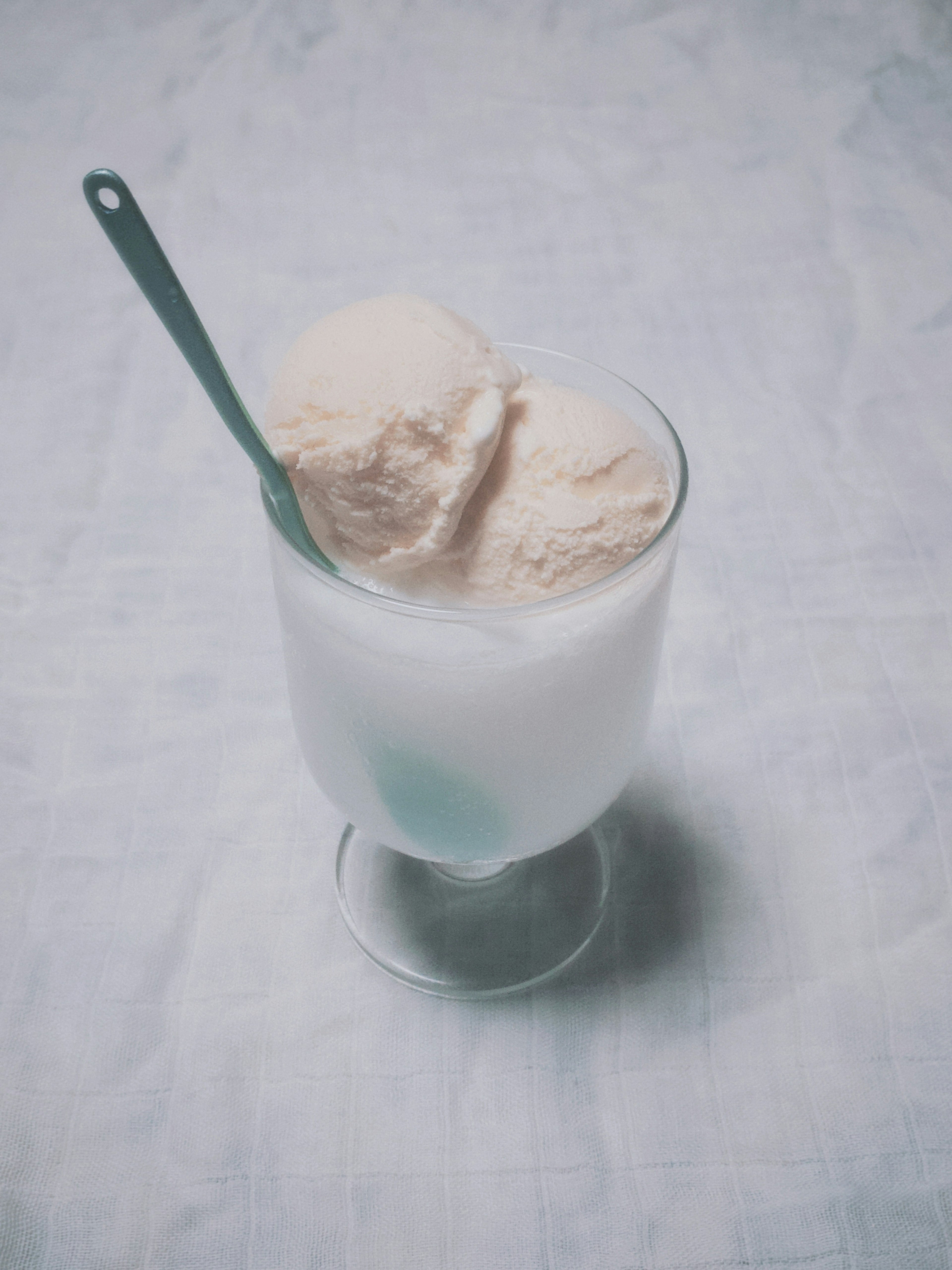 Ein Glas mit zwei Kugeln Eis und einem blauen Löffel