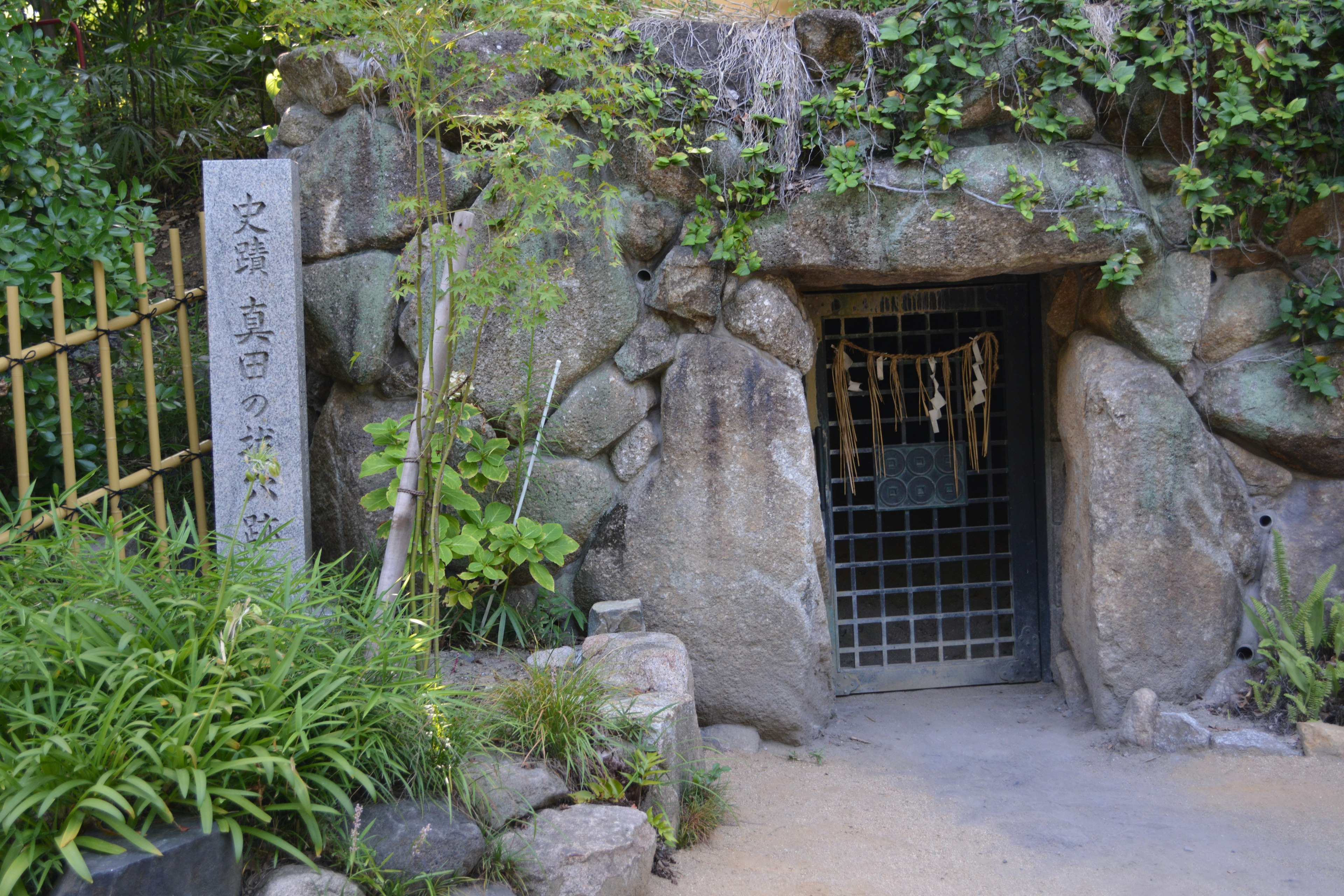 Entrada de piedra rodeada de vegetación con una reja de metal