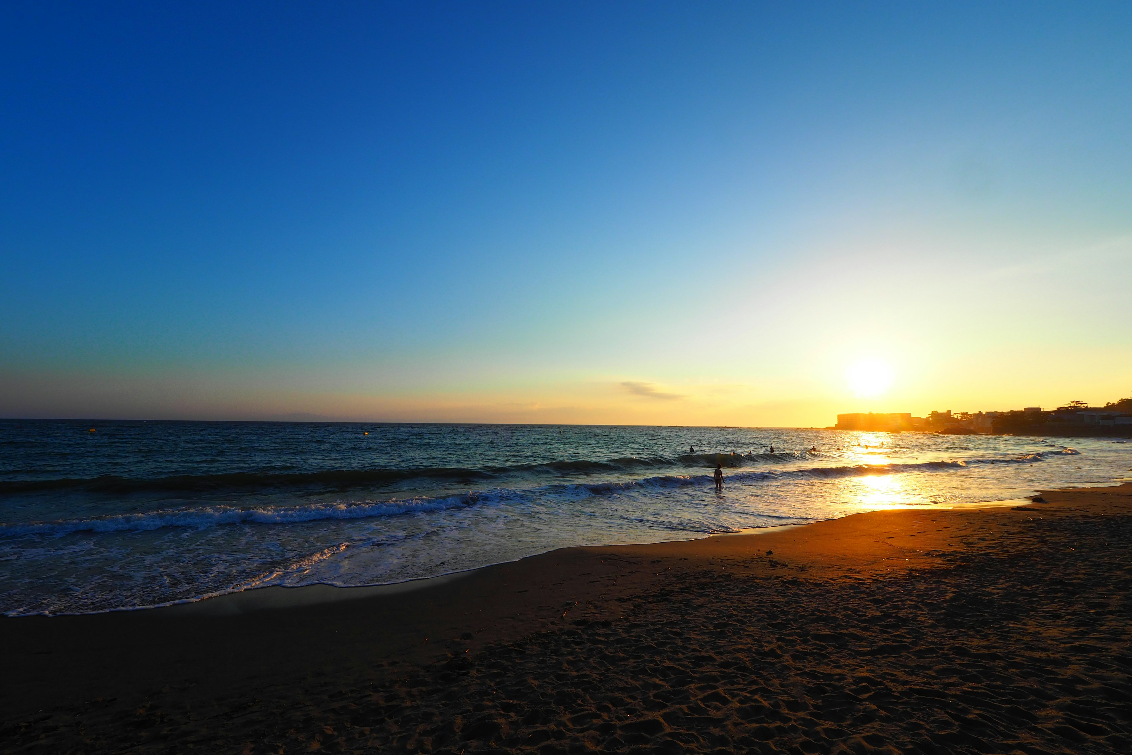 ทิวทัศน์พระอาทิตย์ตกที่ชายหาดมีคนอยู่ในมหาสมุทรสีสันสดใสของท้องฟ้า