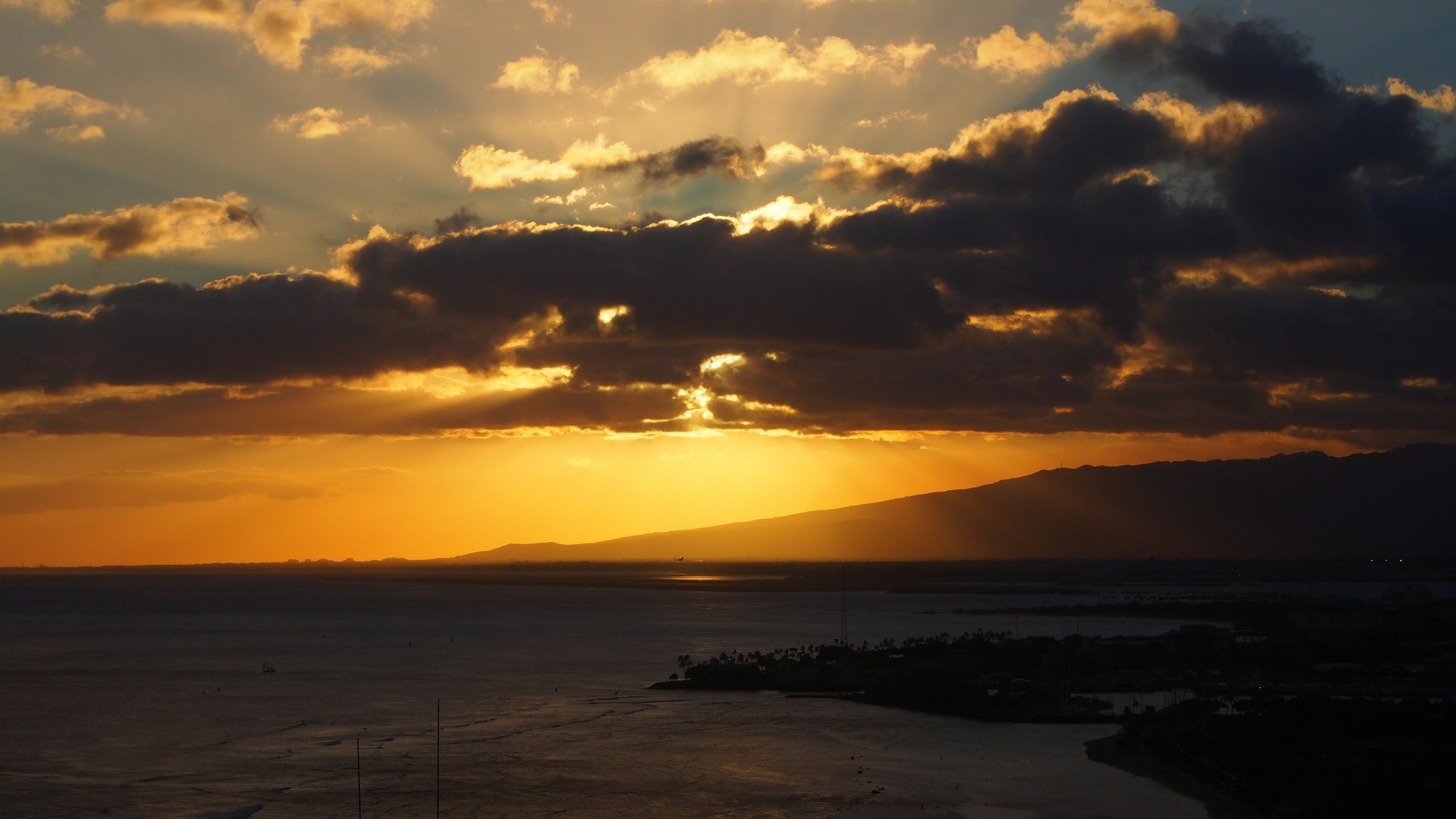 Sunset over the ocean with orange light breaking through clouds and mountains in the background