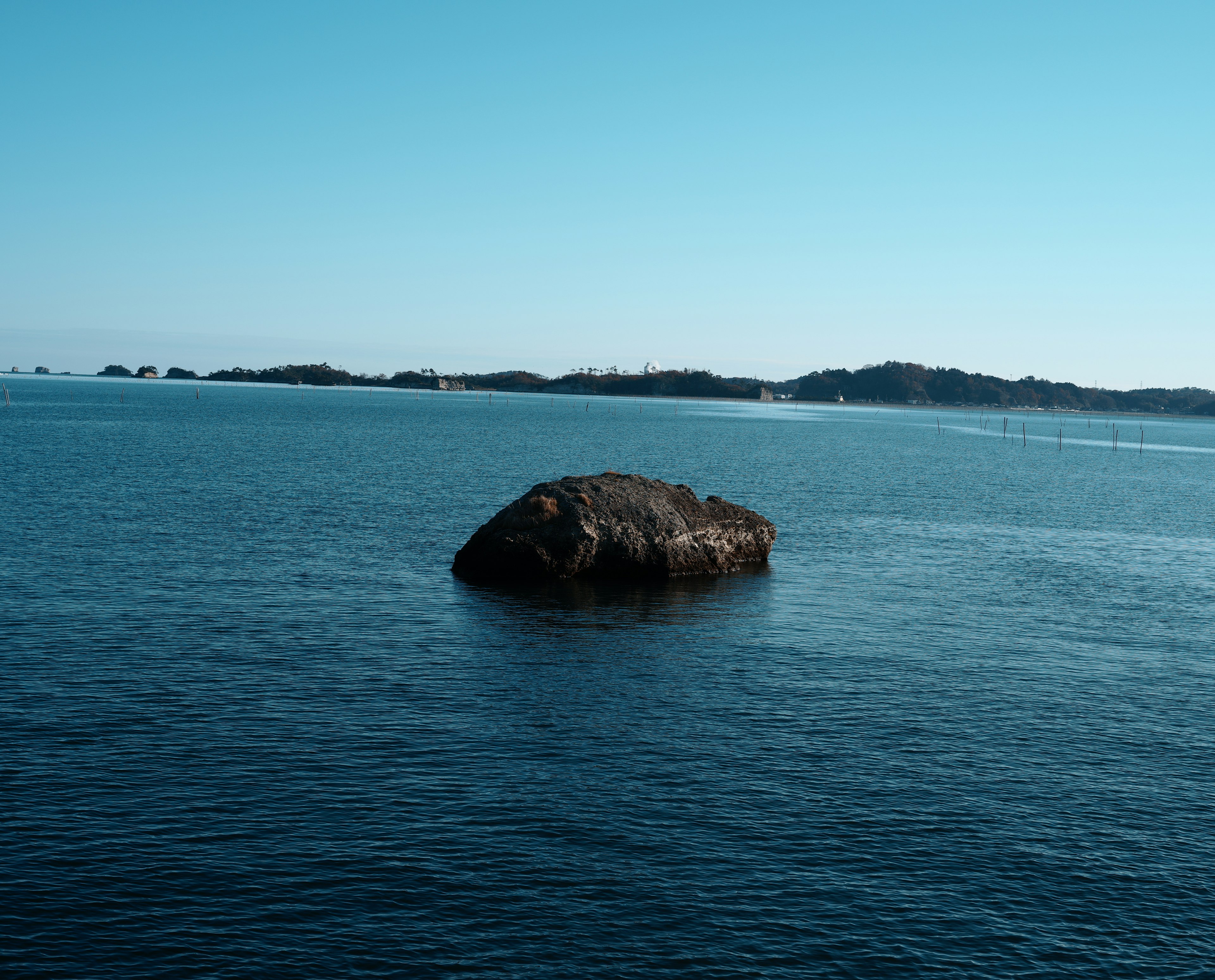 Großer Felsen, der in einem blauen Meer mit fernen Inseln schwimmt