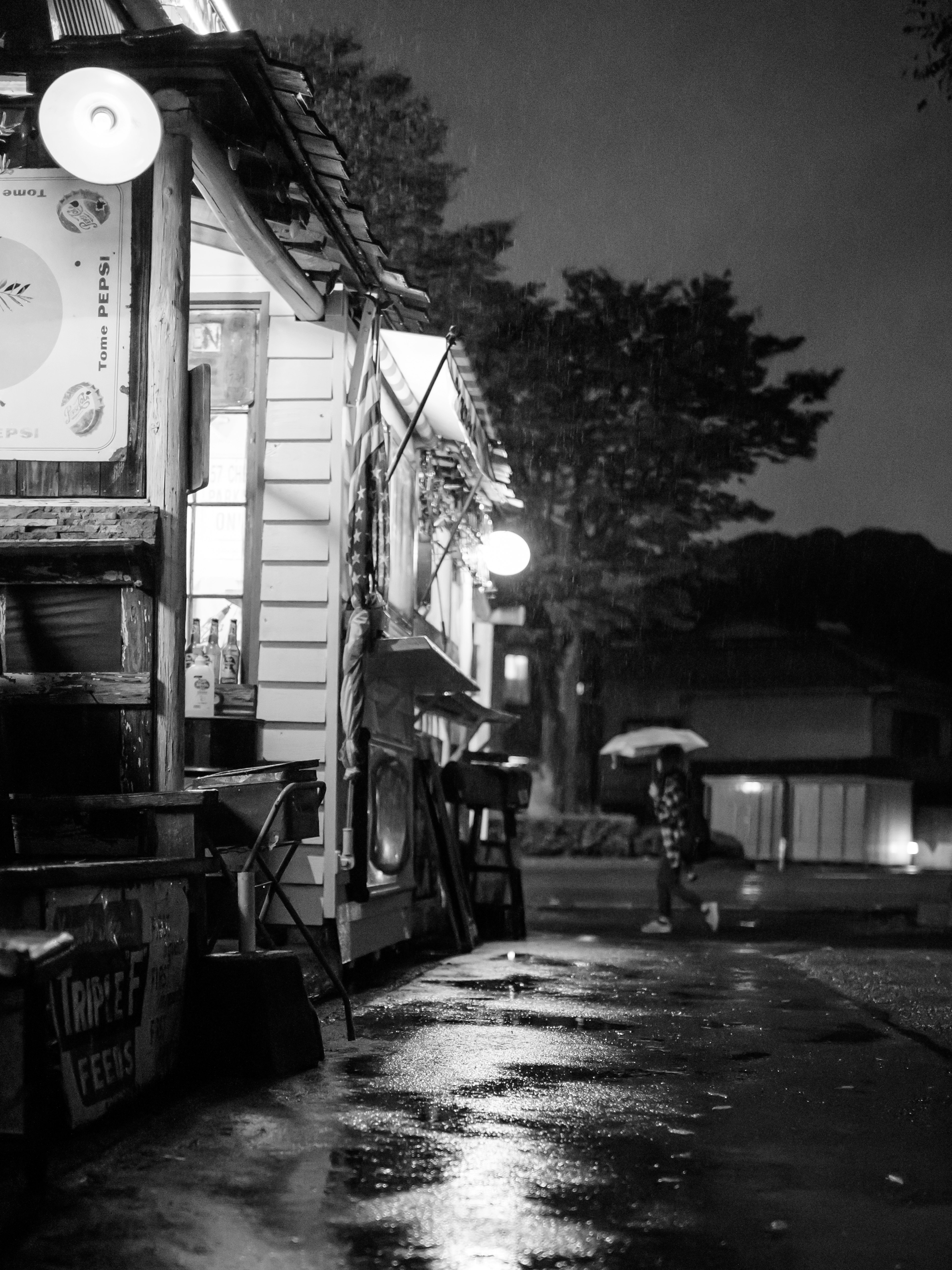 Straßenimbiss bei Nacht mit einer Person, die einen Regenschirm hält