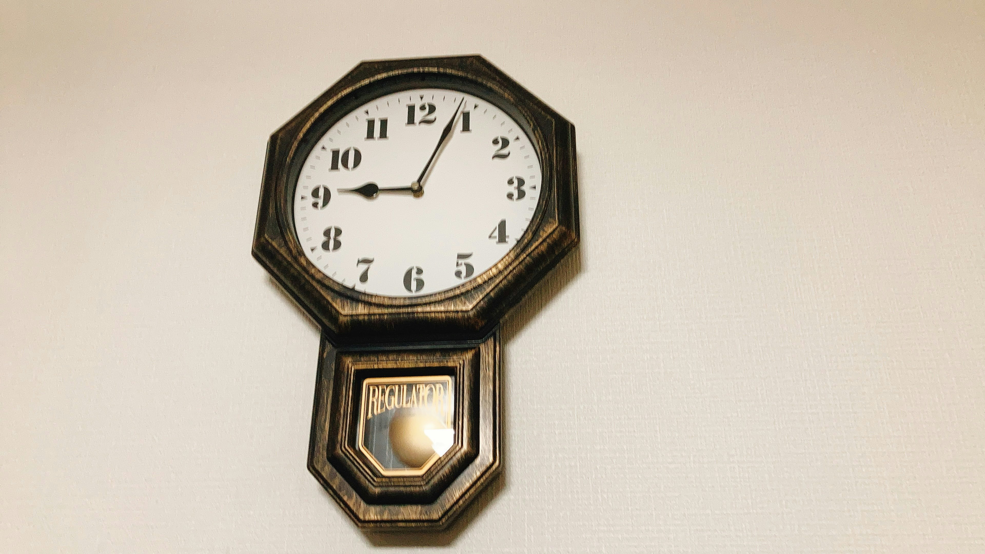 An octagonal wall clock with a white face hanging on a white wall