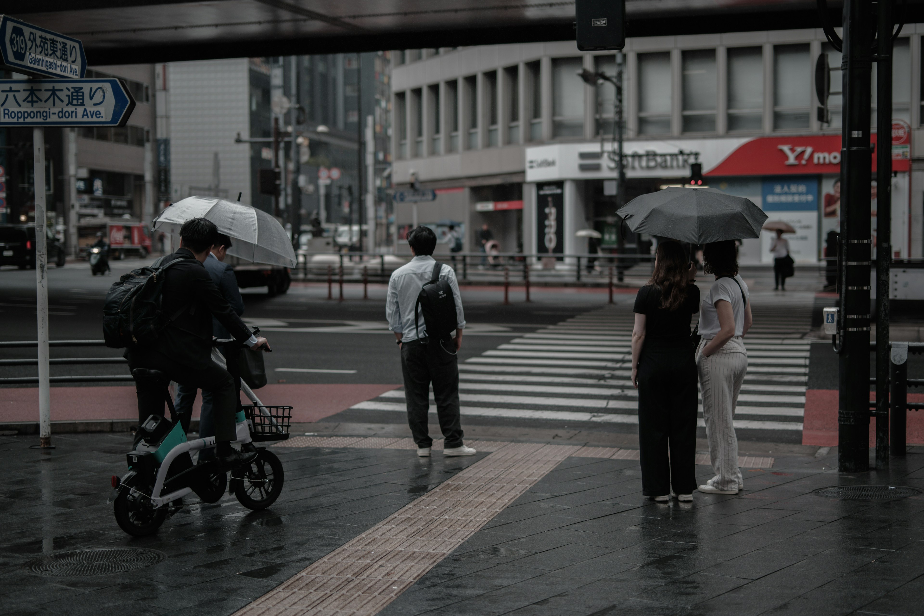 雨の日の交差点で傘を持つ人々と自転車に乗る子供