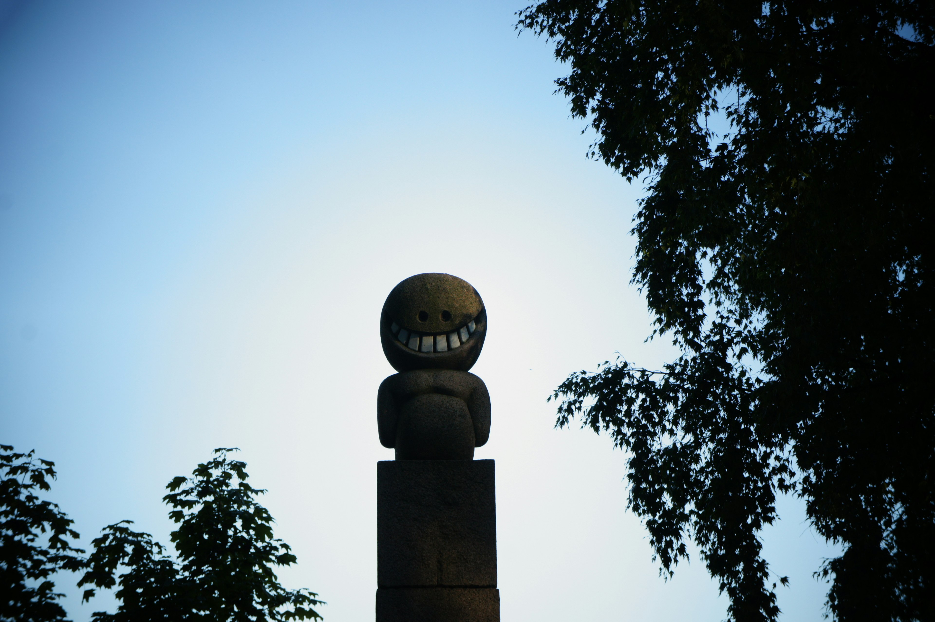 Escultura de madera en silueta contra el cielo con una cara sonriente