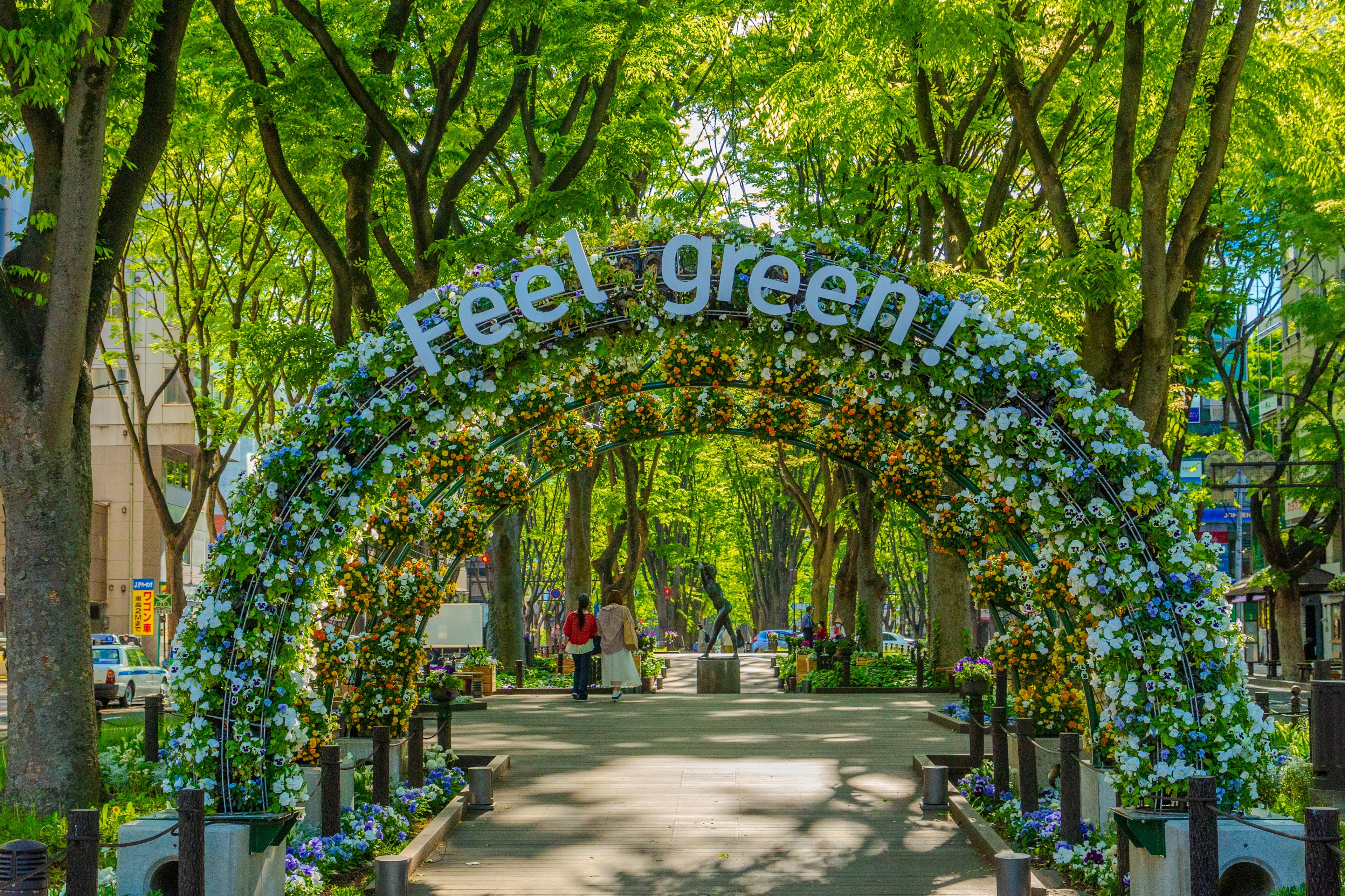 Una scena di parco con un arco decorato di fiori e il testo 'Feel green'