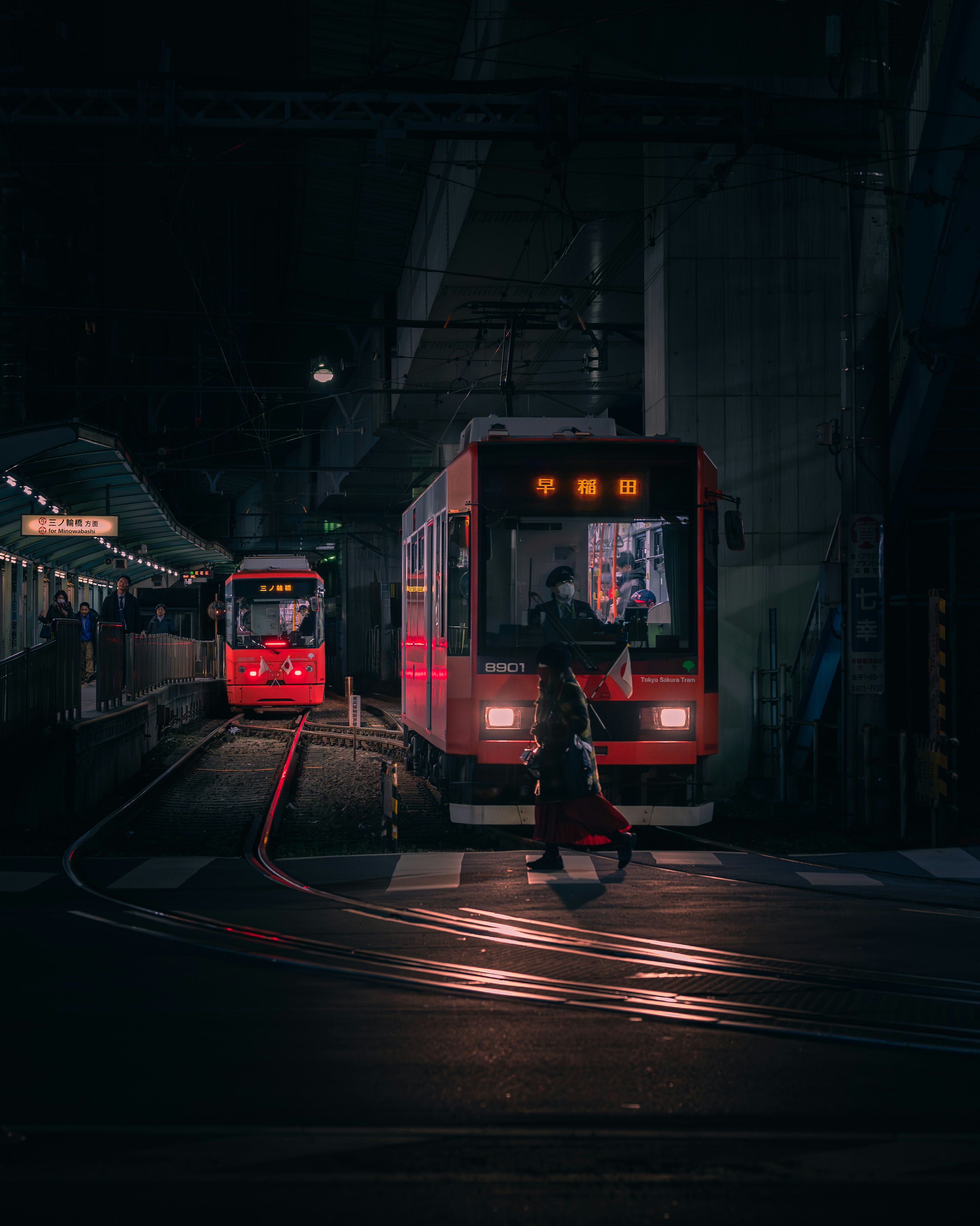 暗い駅での赤い電車とレールを渡る人物