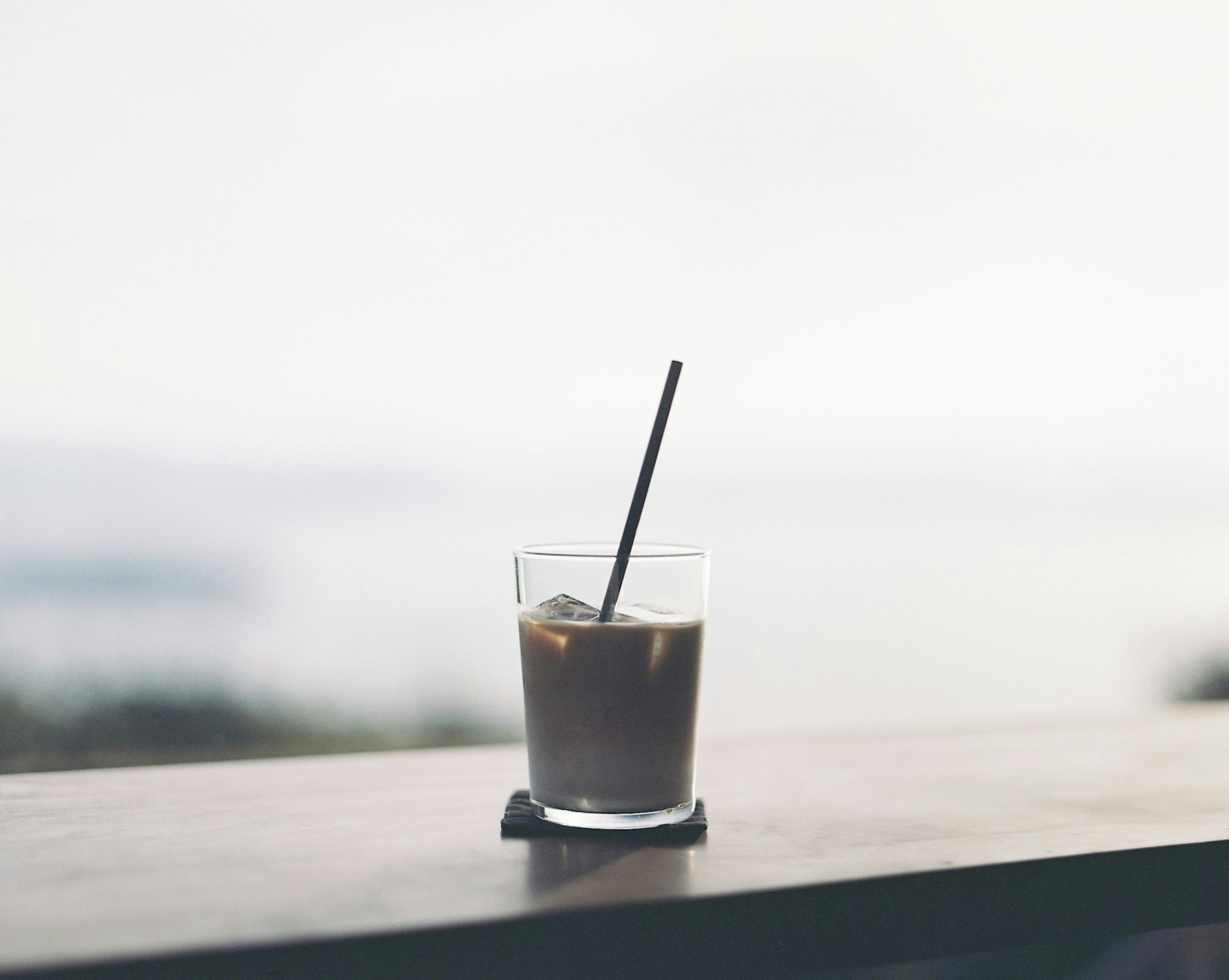 Vaso de café helado con una pajilla sobre una superficie de madera junto a la ventana