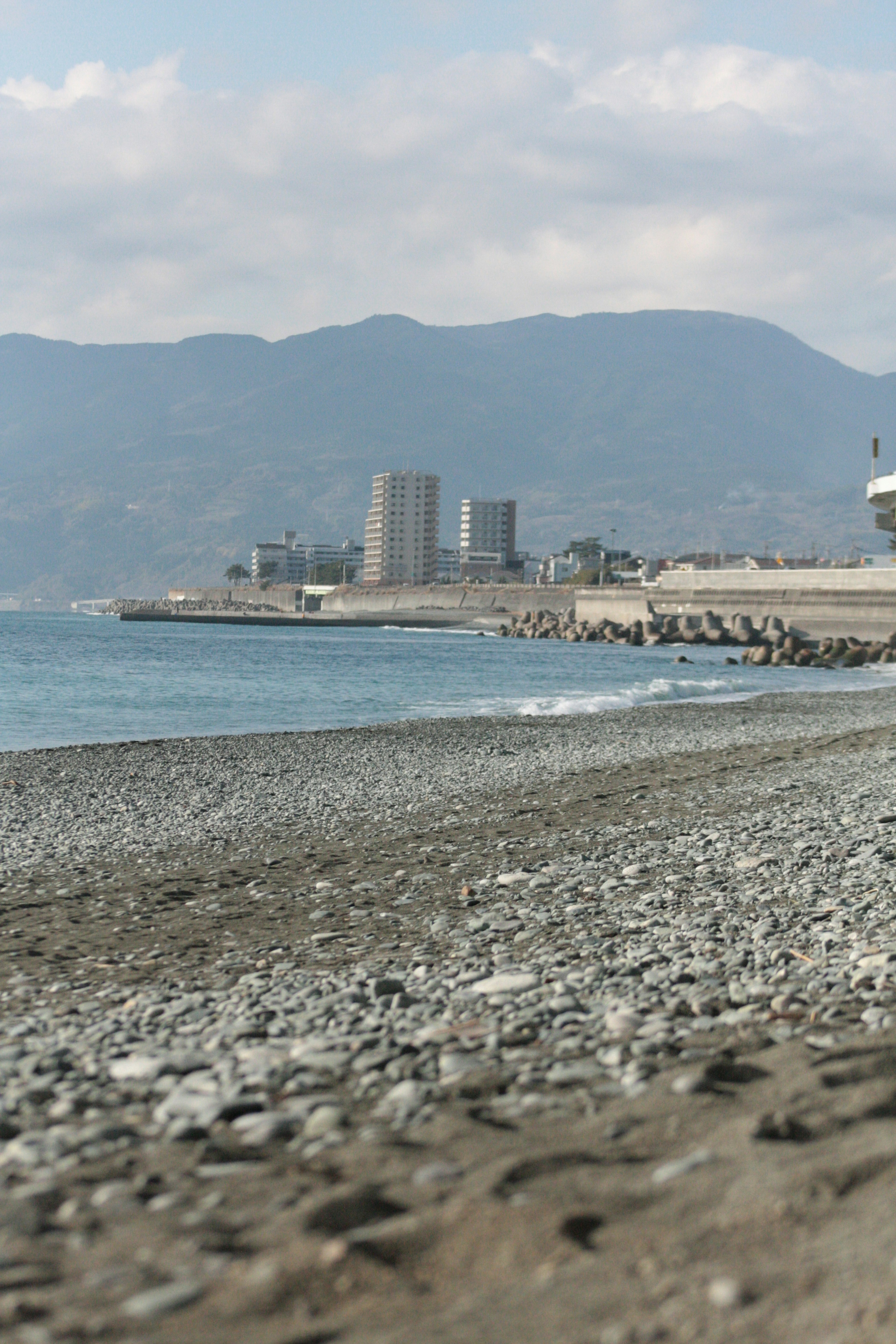 Vista costiera con ciottoli e mare blu Montagne e edifici sullo sfondo