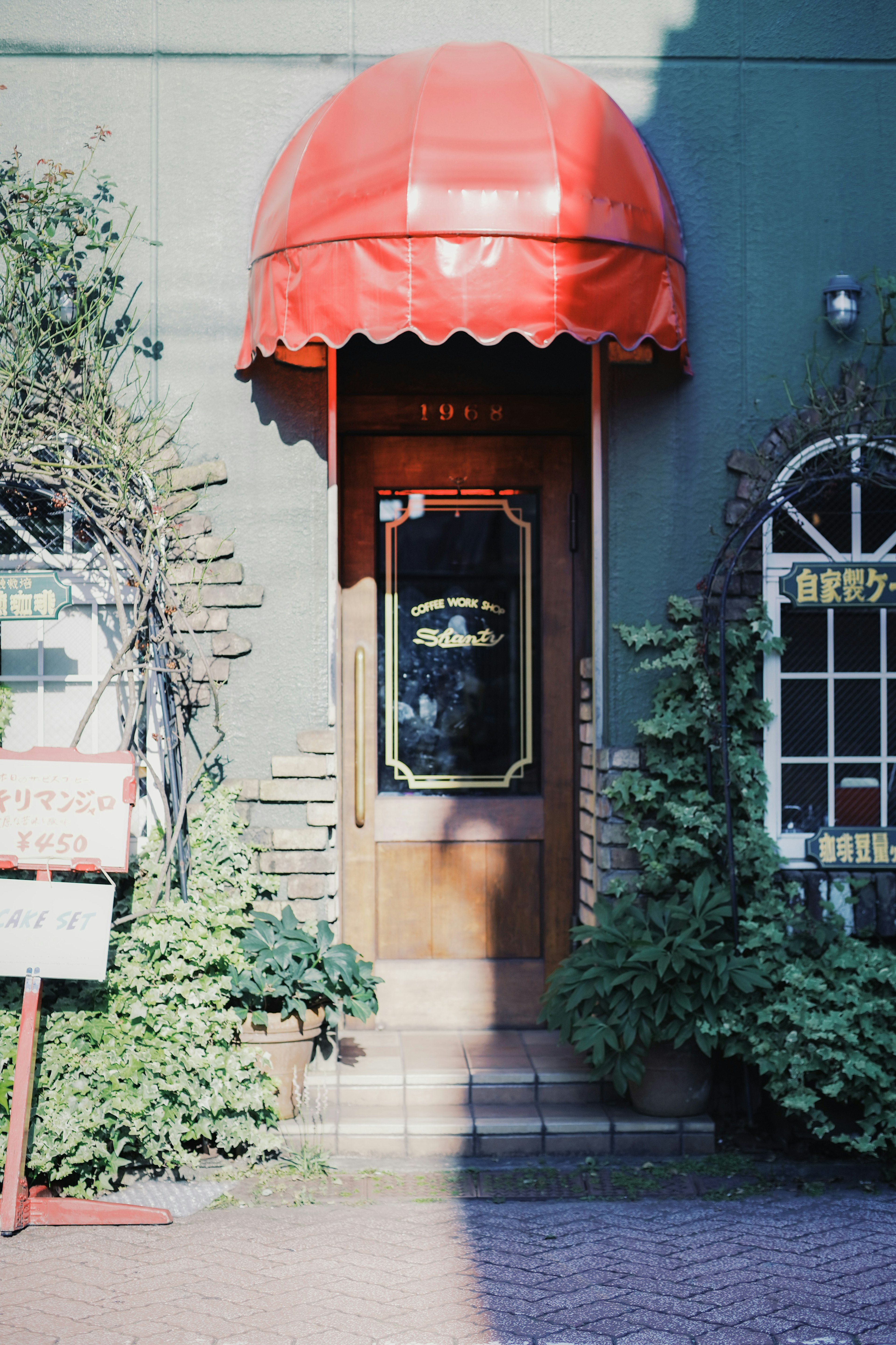 Entrée d'un magasin avec un auvent rouge et des murs verts entourés de plantes