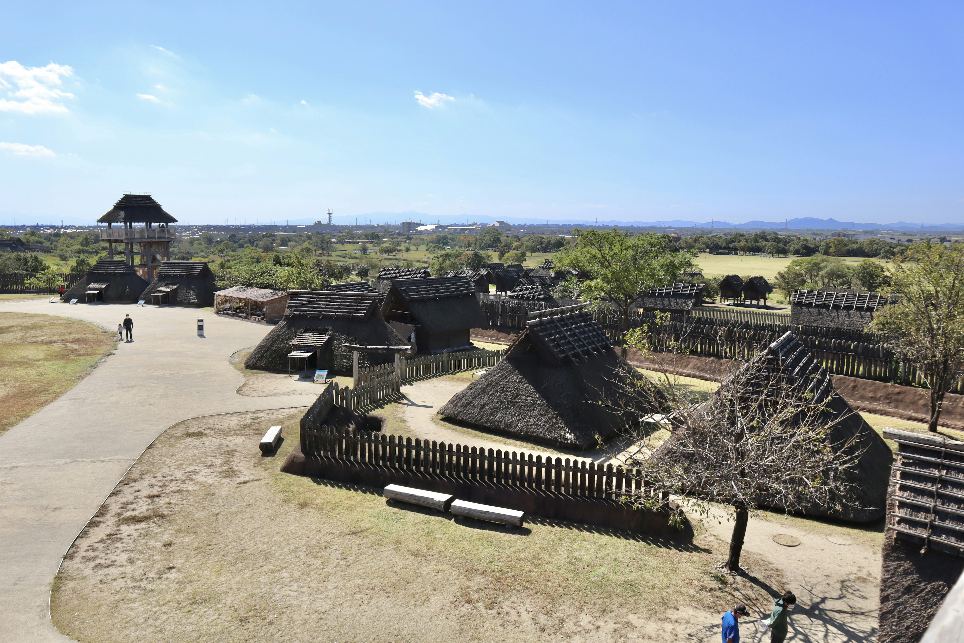 Scène d'un village reconstitué avec des huttes traditionnelles sous un ciel bleu clair