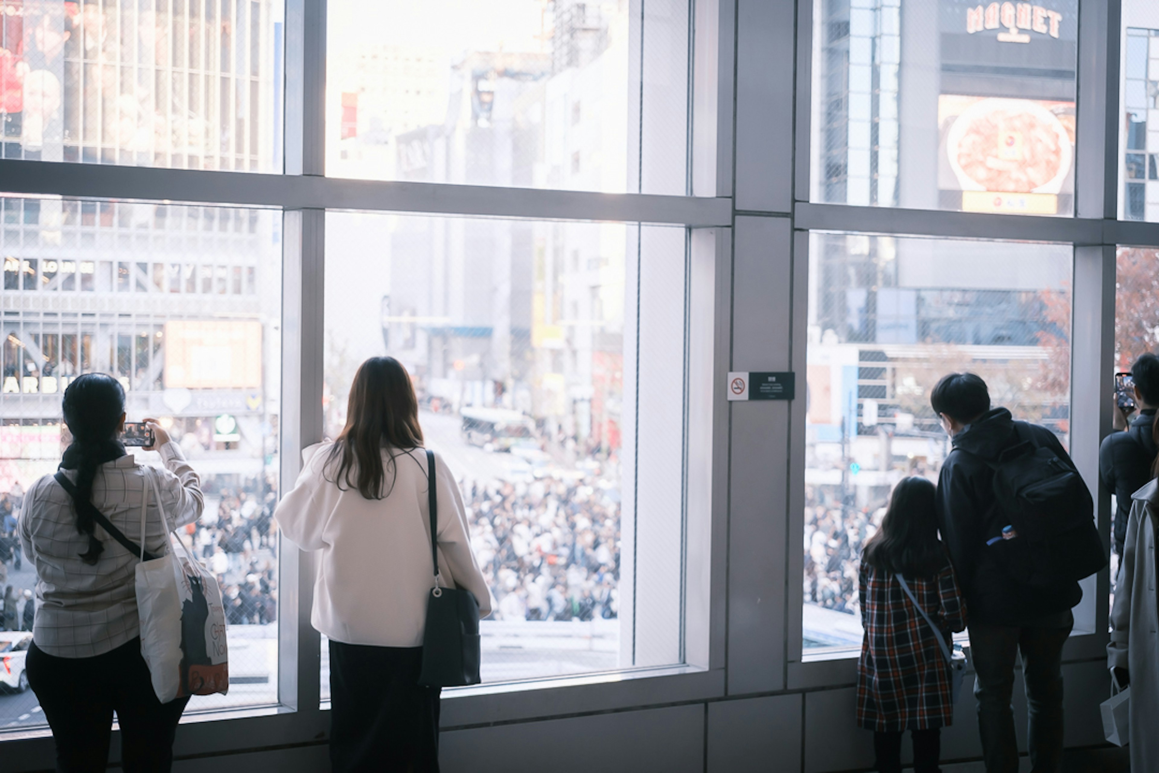 Persone che guardano fuori dalla finestra verso la folla a Shibuya Crossing