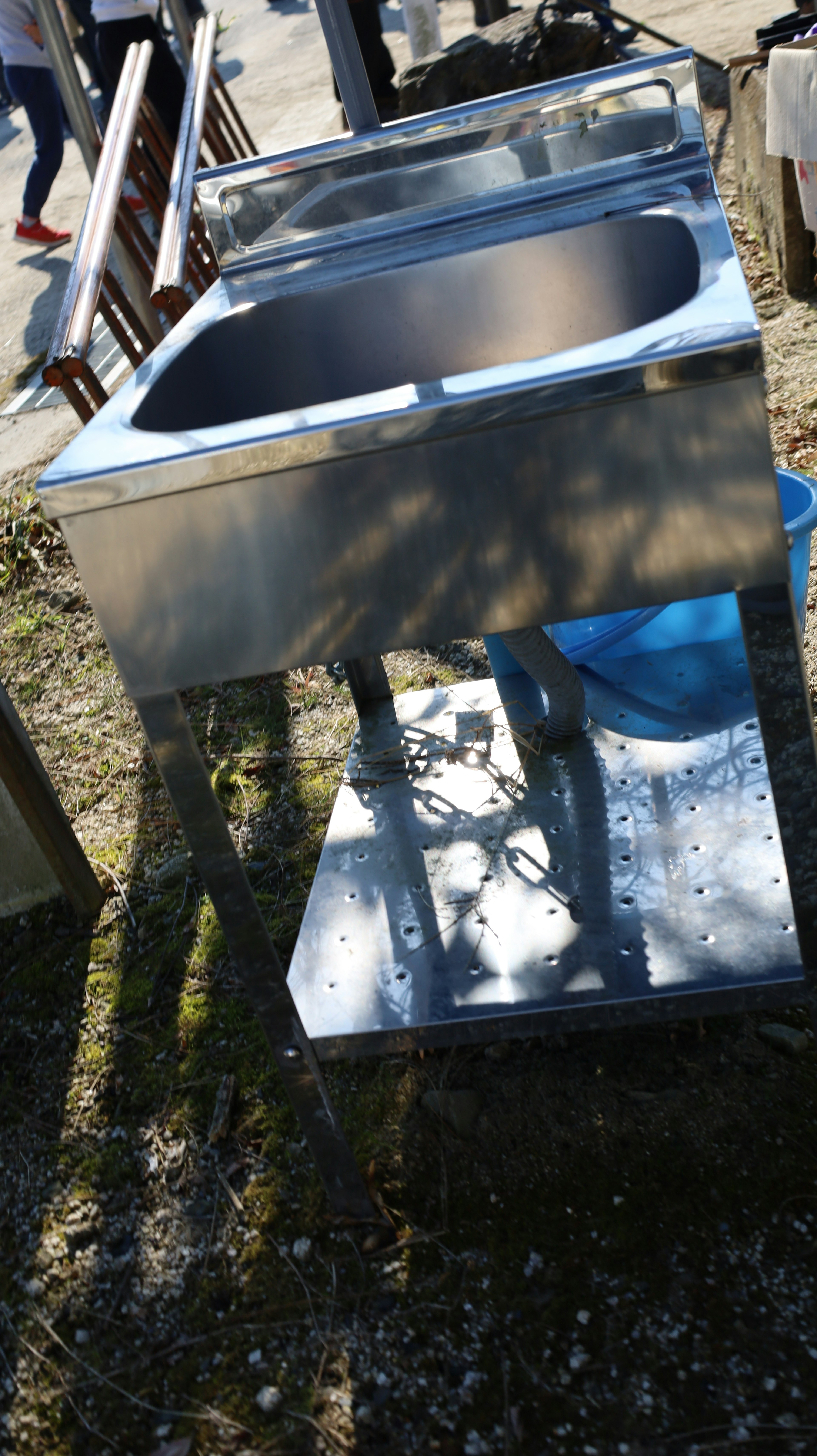 Metal sink placed outdoors with a blue bucket nearby