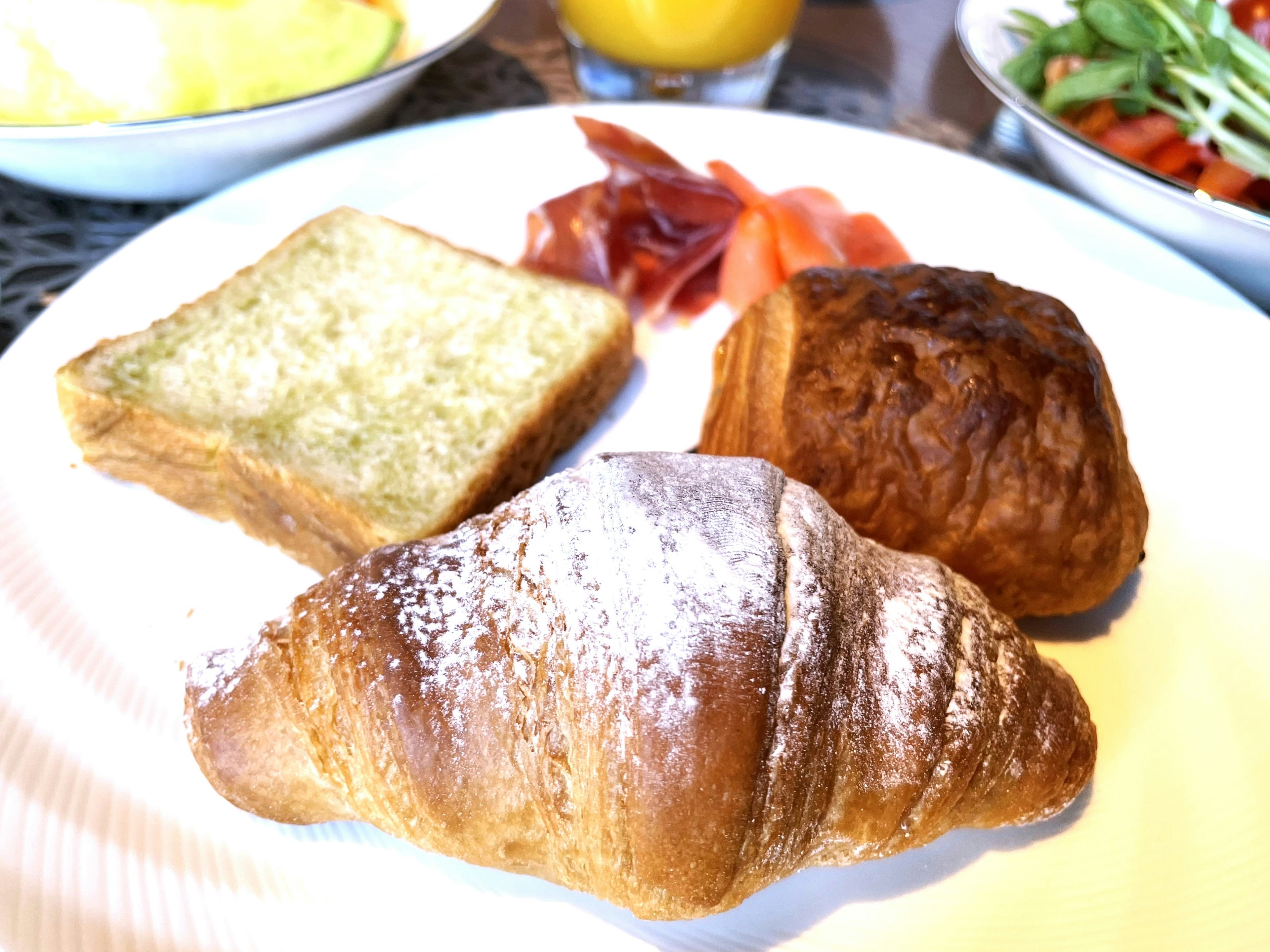 朝食のプレートにトースト、クロワッサン、ペストリー、野菜サラダが盛り付けられている