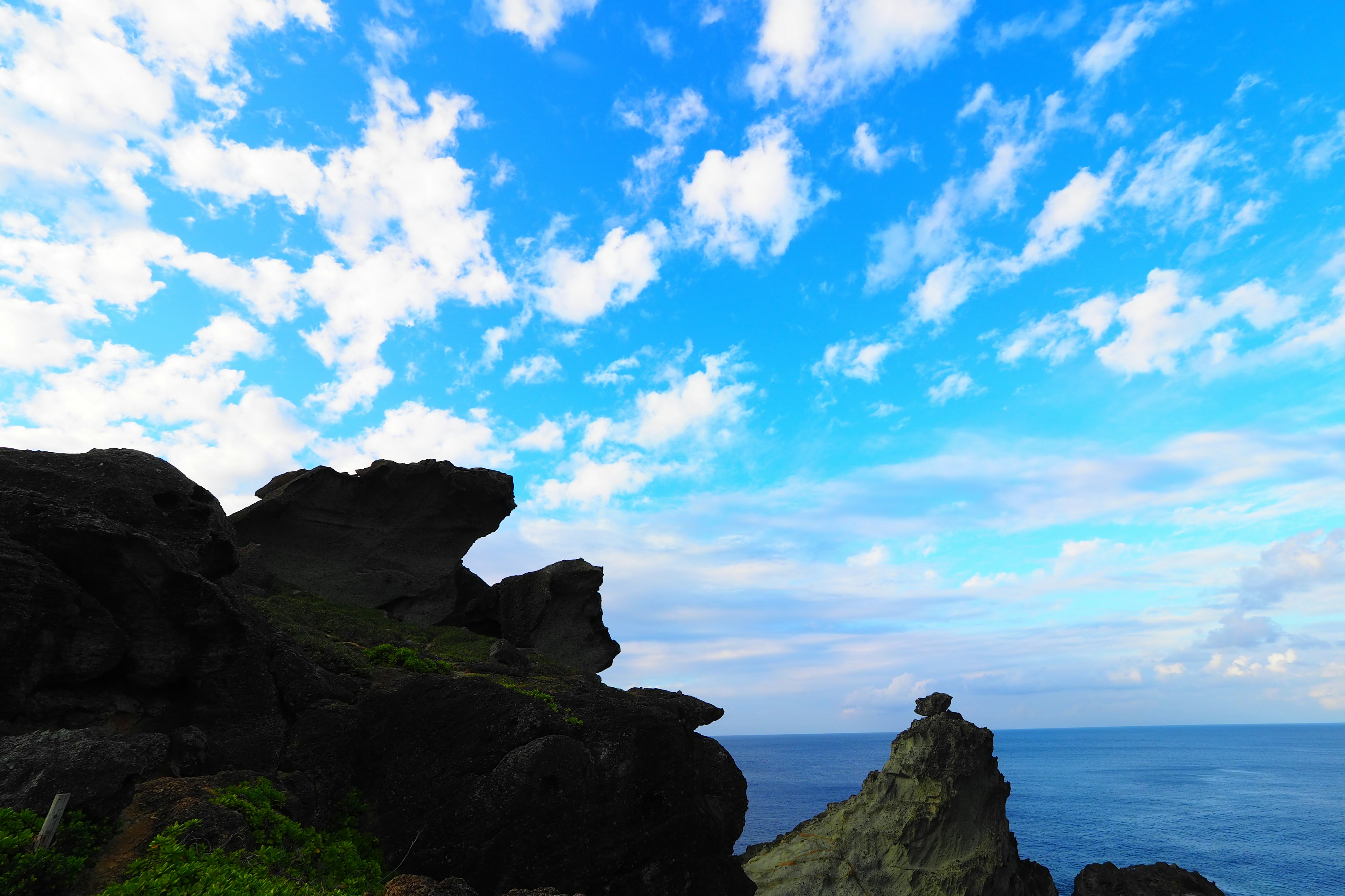 Silhouette di rocce contro un cielo blu con nuvole bianche sopra il mare