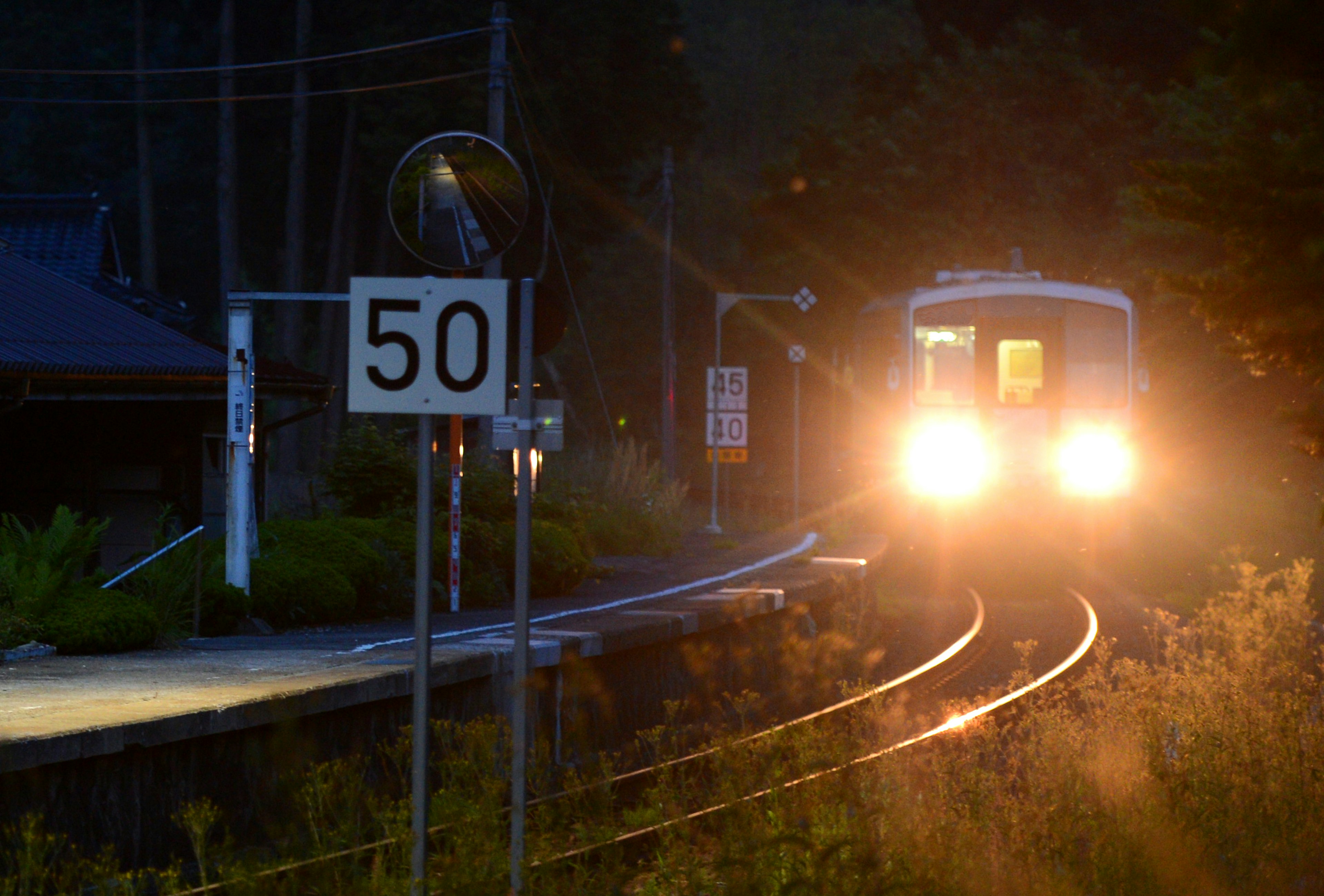 Kereta mendekati stasiun di malam hari dengan lampu depan dan rambu batas kecepatan 50